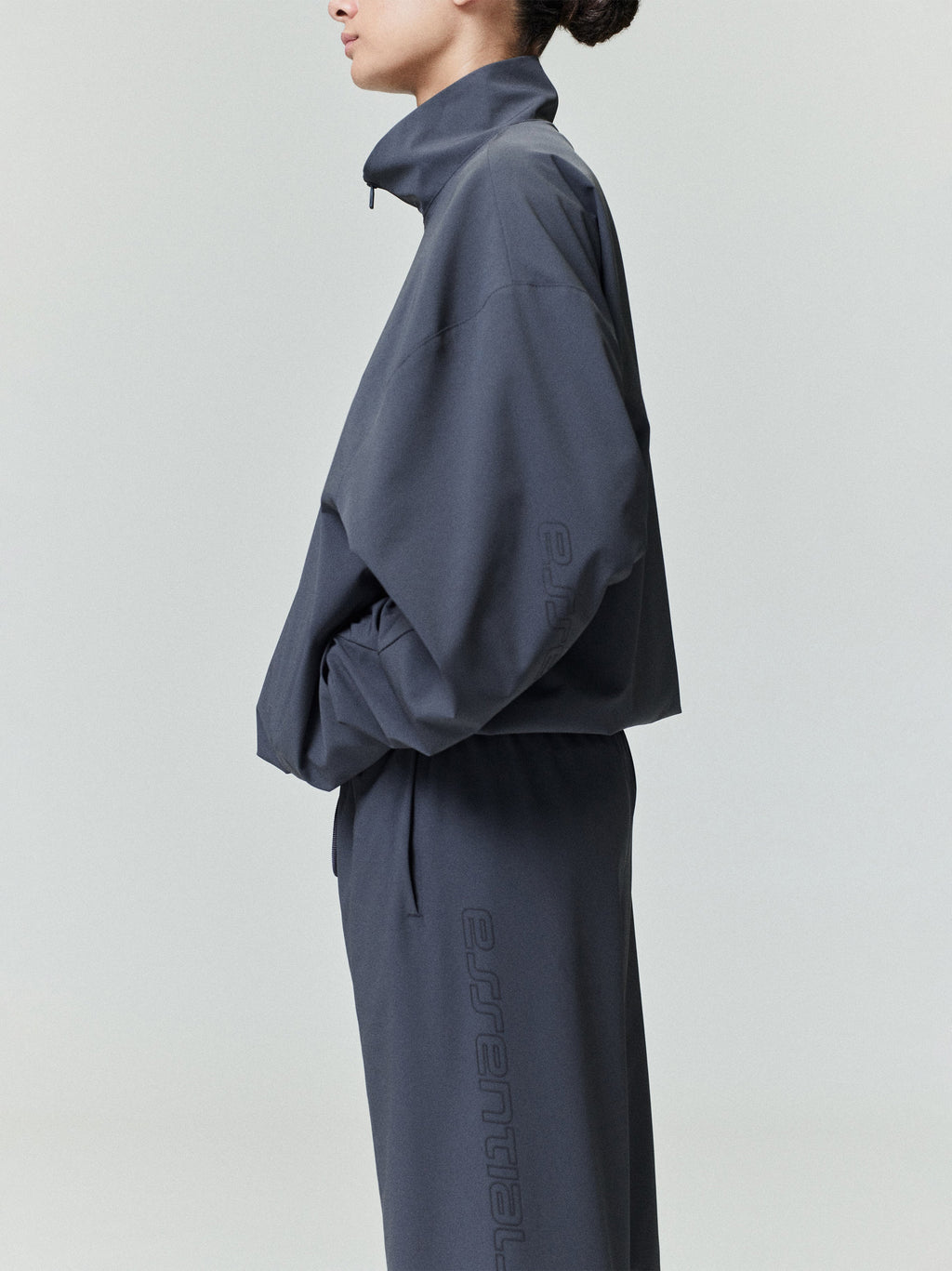 Woman in dark navy nylon half-zip track jacket and matching pants standing sideways with hands in pockets