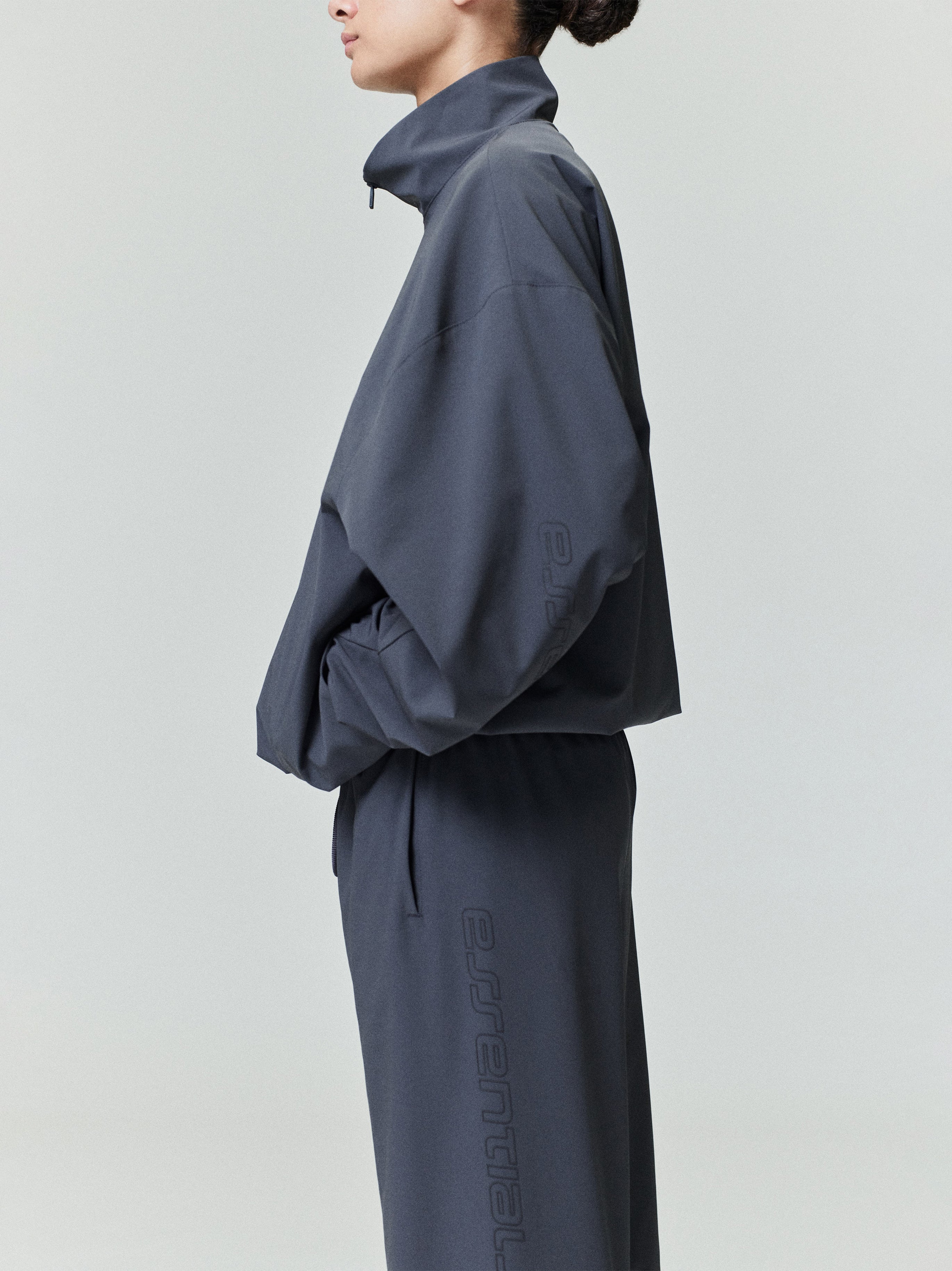 Woman in dark navy nylon half-zip track jacket and matching pants standing sideways with hands in pockets
