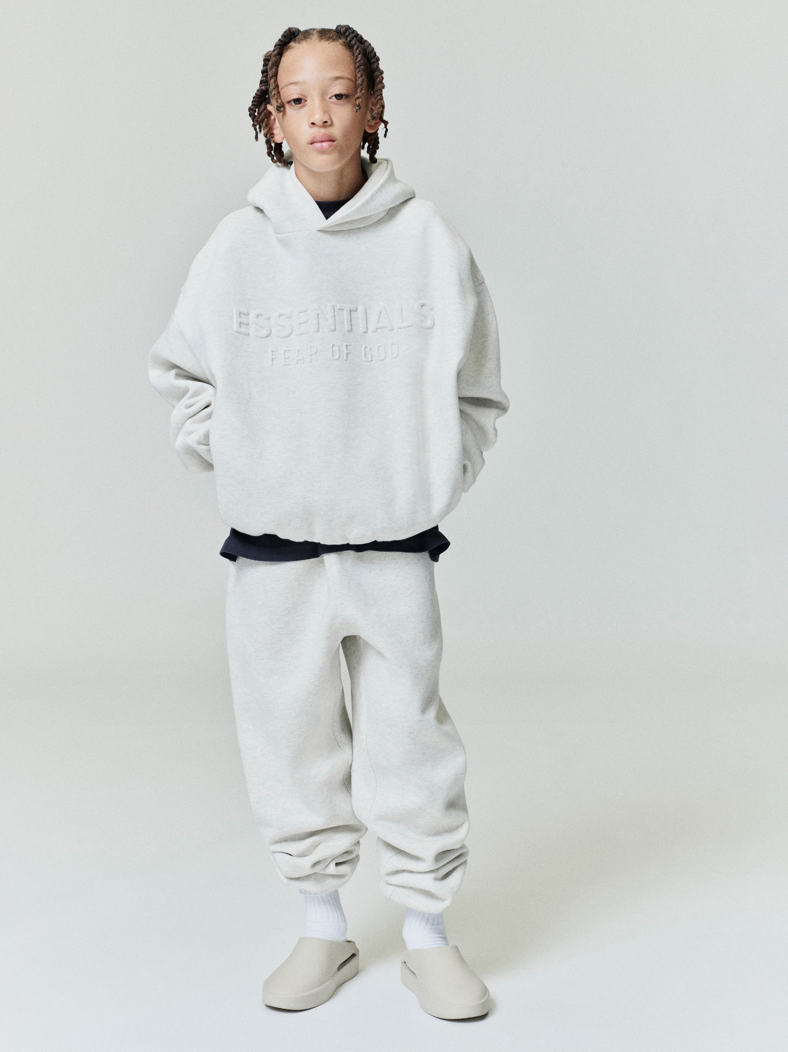 Front view of oatmeal Kids Embossed Classic Hoodie with subtle raised ESSENTIALS Fear of God logo, gallery position 0, file 0001_HO25_K_L76_4065.jpg