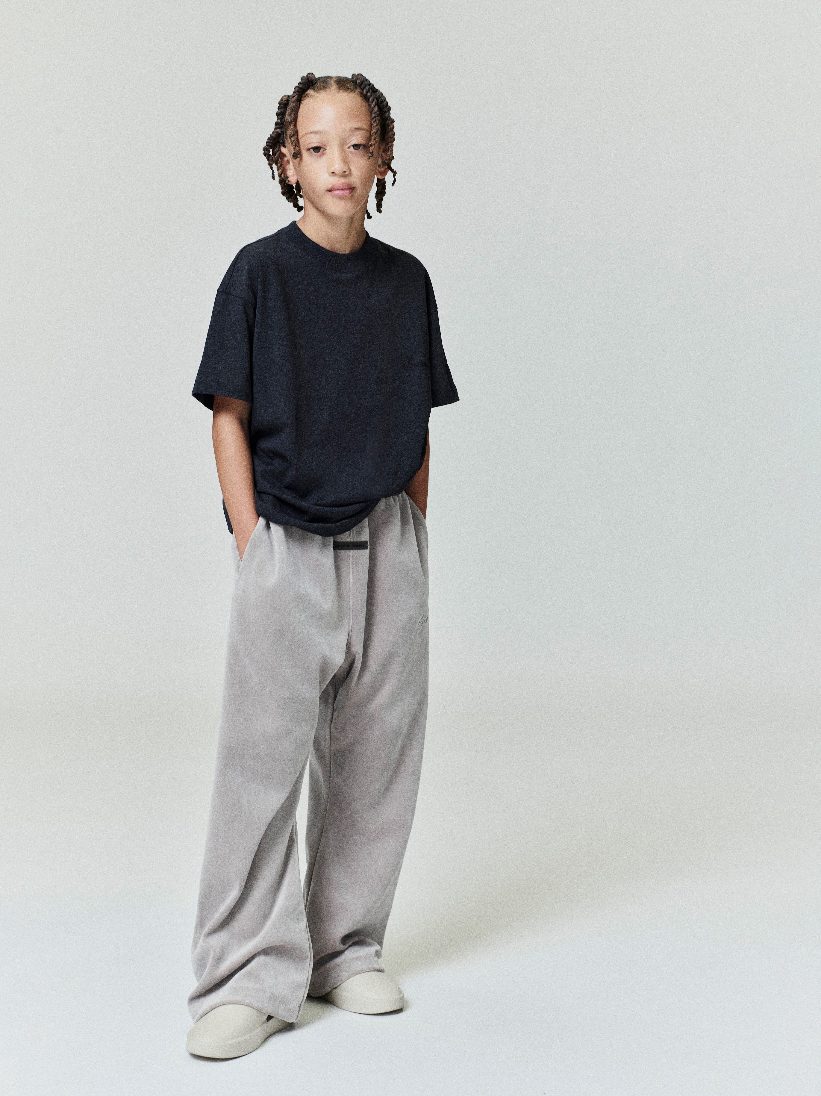 Full body view of child wearing black Kids Embroidered Essential Tee with relaxed fit, hands in pockets, gallery position 0
