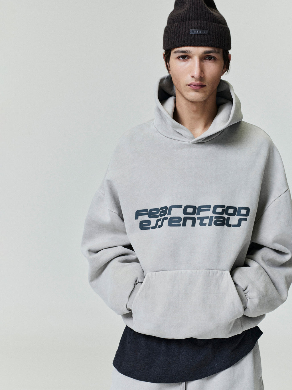 Front view of light gray Heavy Fleece 90s Hoodie with bold Fear of God Essentials logo worn with dark beanie 0008_HO25_F_L54_P31_2325.jpg
