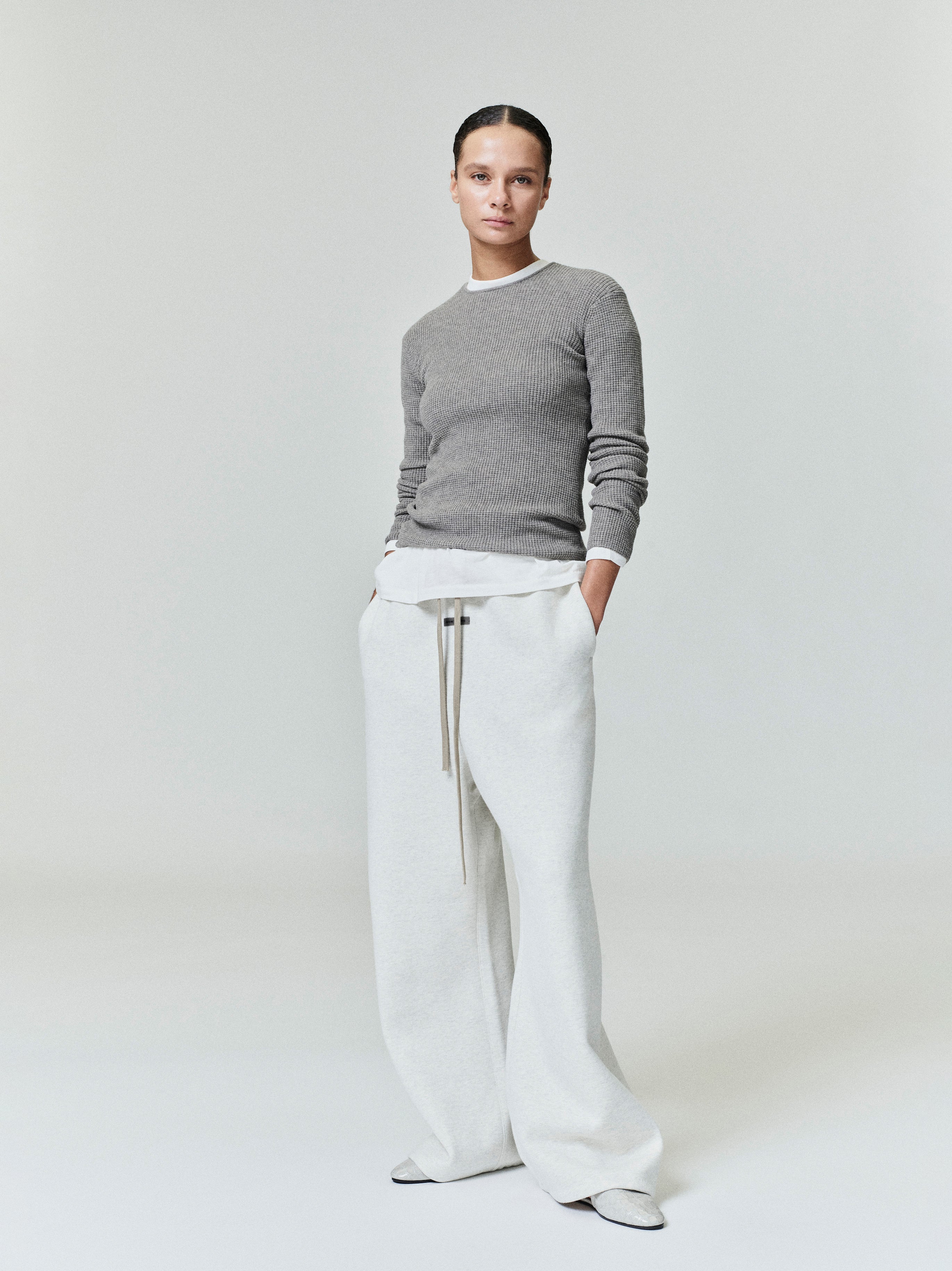 woman wearing grey waffle knit long sleeve top with white layered hem and cream wide-leg pants standing