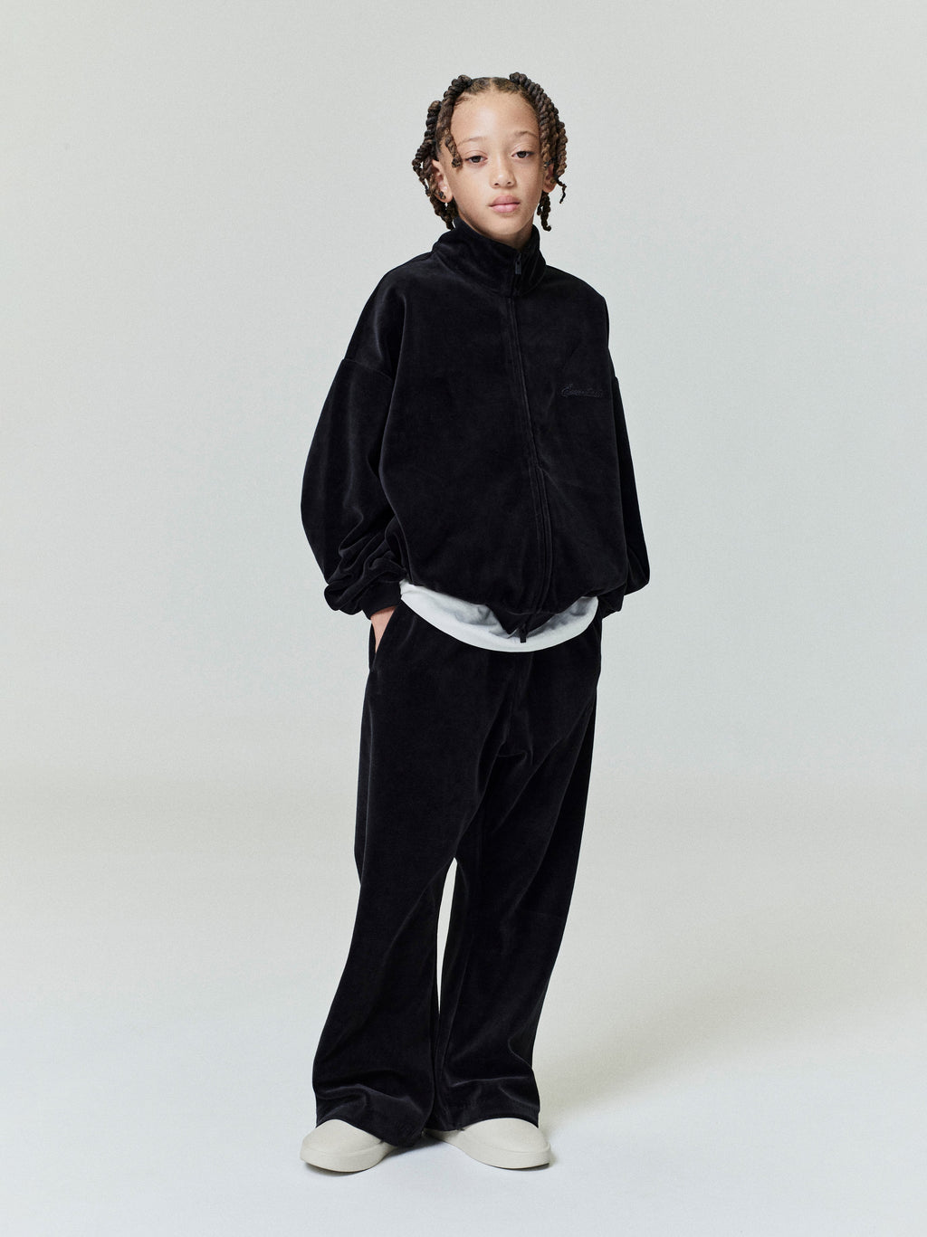 Child wearing black kids velour flare sweatpant with relaxed fit and matching zip-up jacket against plain background