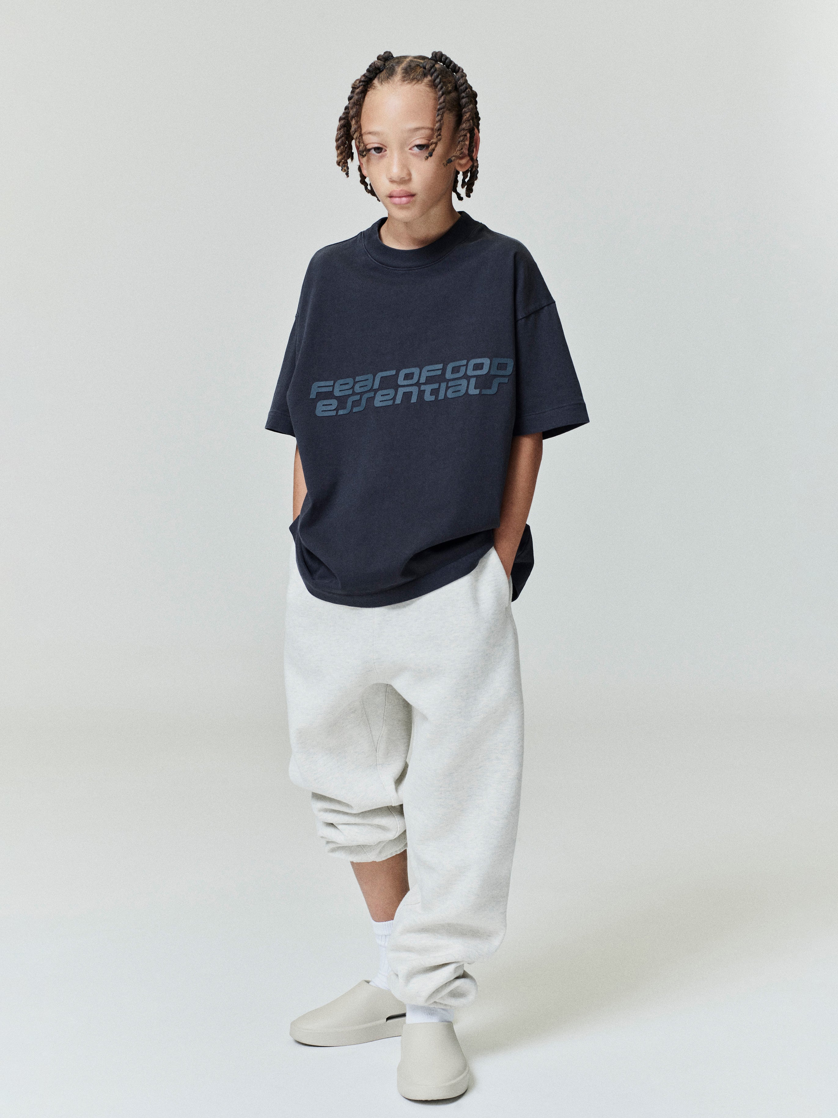 Child wearing navy Kids Classic Short Sleeve Tee with subtle logo print, standing front view, gallery position 0, file 0009_HO25_K_L75_4000.jpg