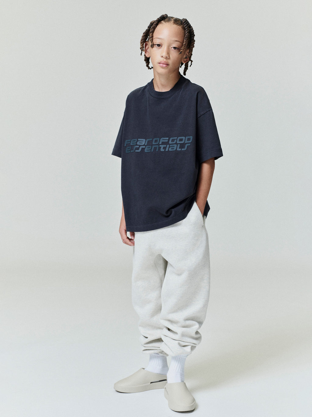 Full front view of child wearing navy Kids Classic Short Sleeve Tee with subtle Fear of God Essentials print, gallery position 0