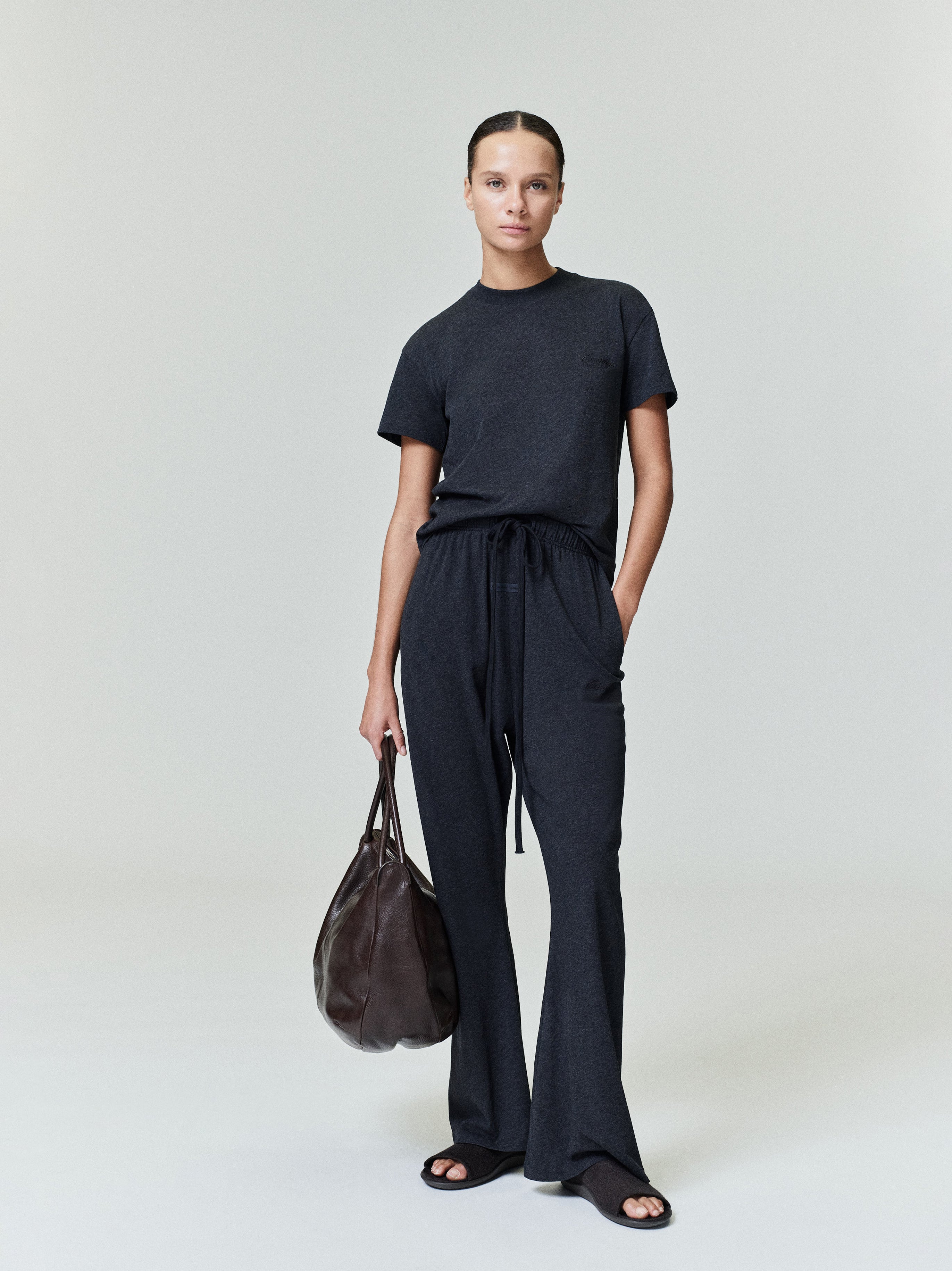Full-length image of woman wearing vintage black Womens Embroidered Classic Tee with matching pants and brown leather bag
