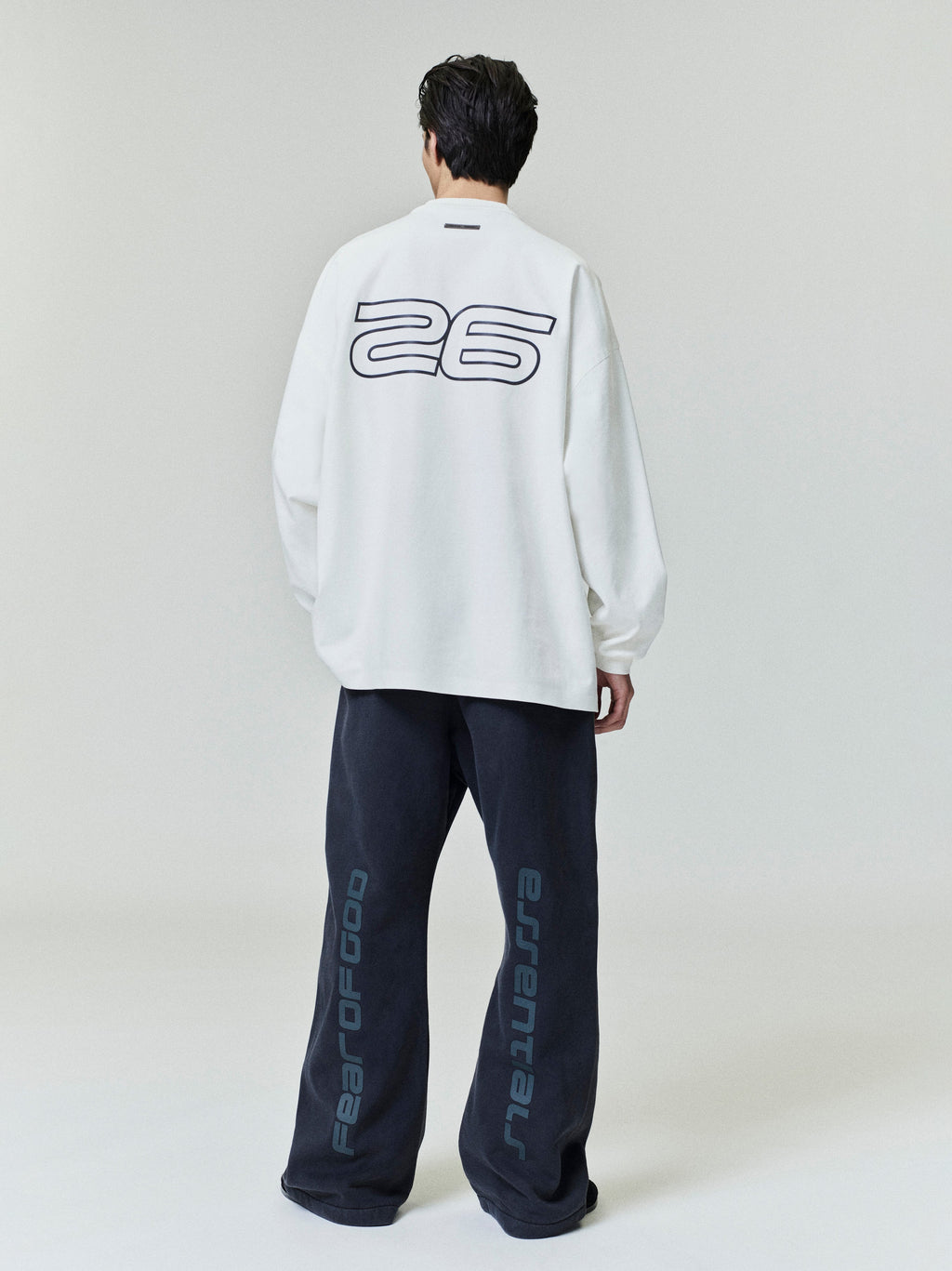 Back view of white Ponte 90s Long Sleeve Tee with large "26" graphic, styled with black pants featuring vertical branding, gallery 0.