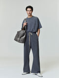 Model wearing dark grey flare sweatpants with beige drawstrings, paired with matching short-sleeve top and carrying gray bag front view