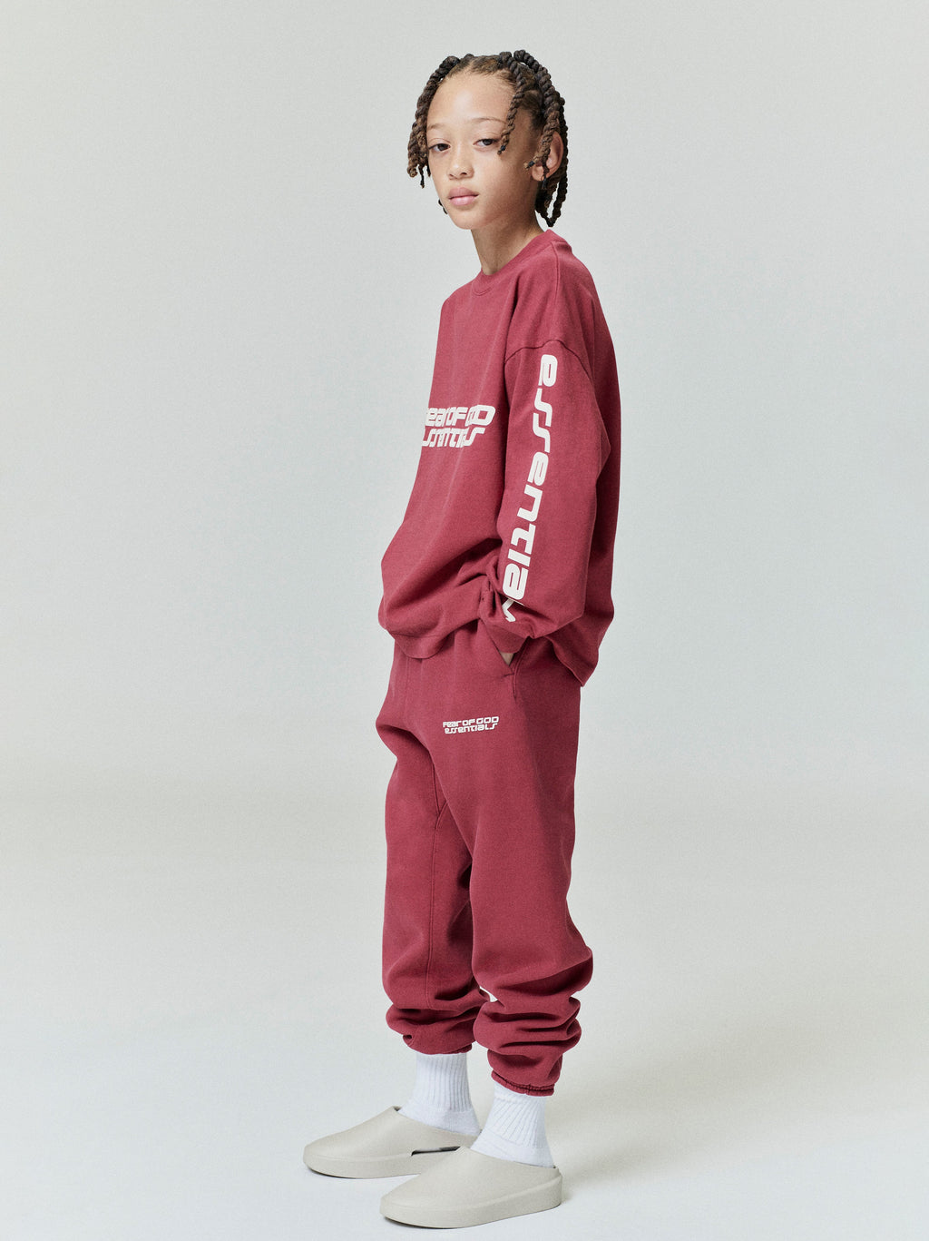 Side view of child wearing crimson Kids Classic Long Sleeve Tee with white essential print on sleeve, gallery position 0, file 0013_HO25_K_L73_3889.jpg