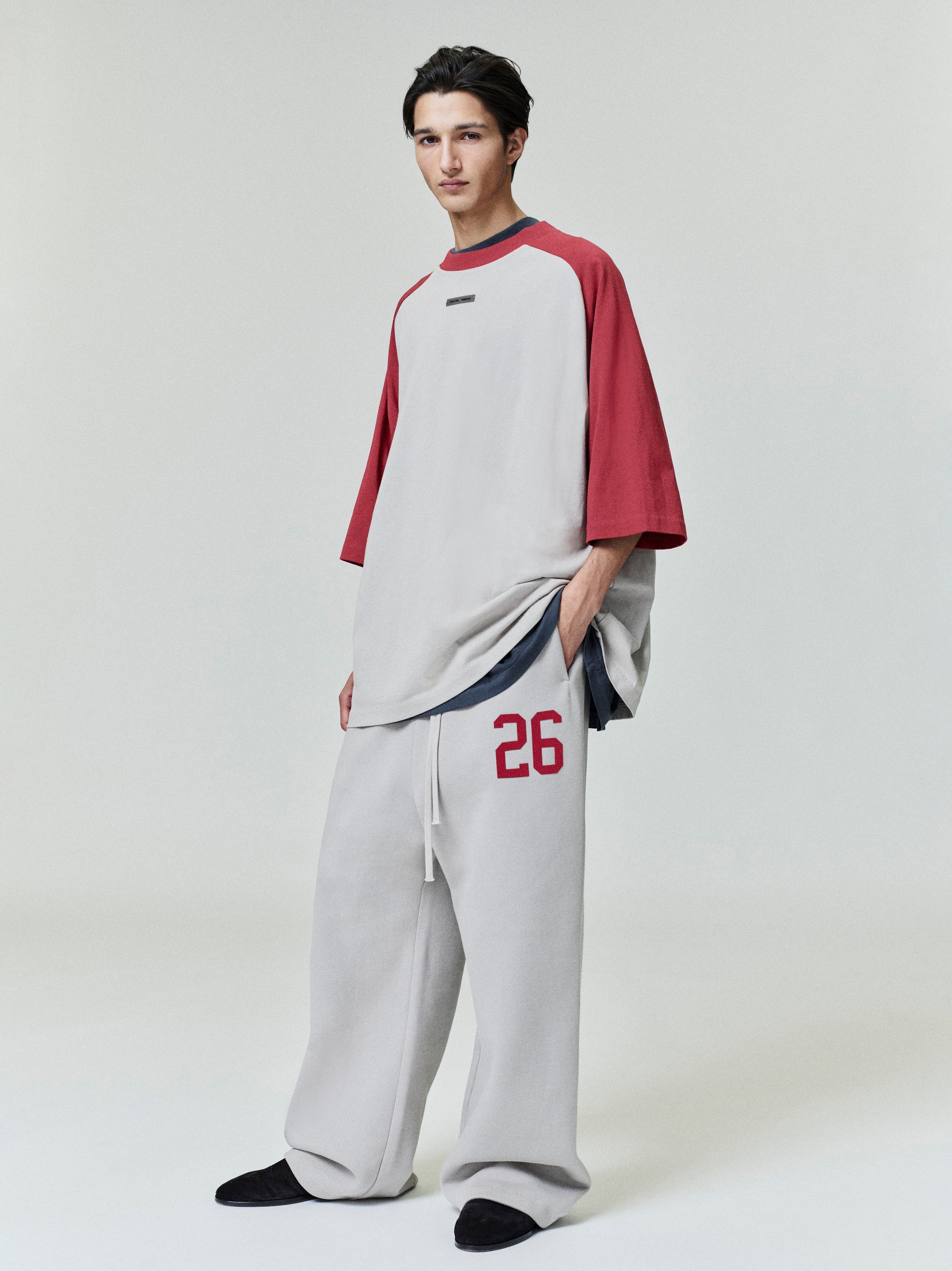 Male model in oversized baseball tee with muted grey body and deep red raglan sleeves, full length studio shot