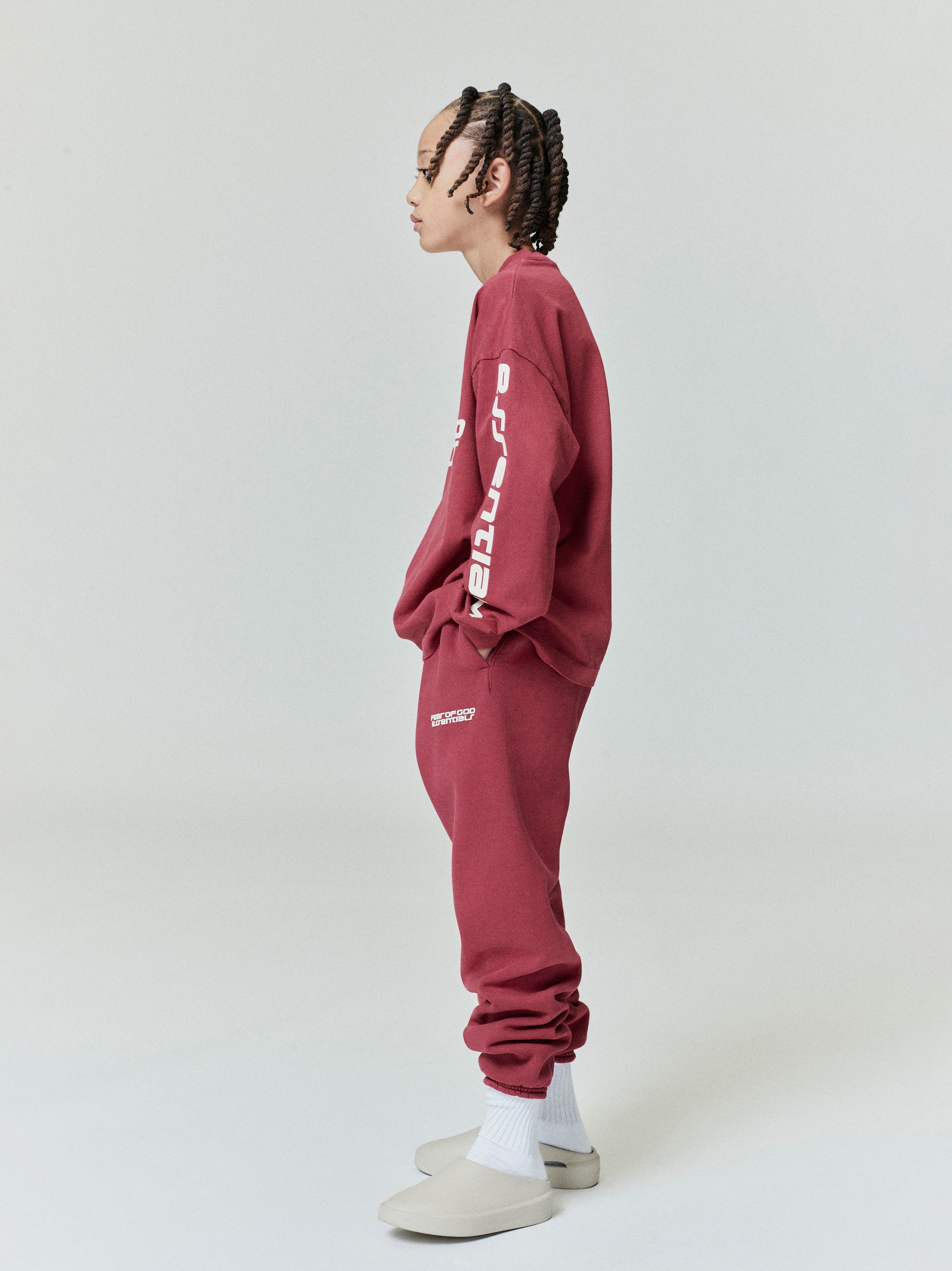 Side profile of child wearing crimson Kids Classic Long Sleeve Tee with white vertical sleeve lettering, gallery position 0