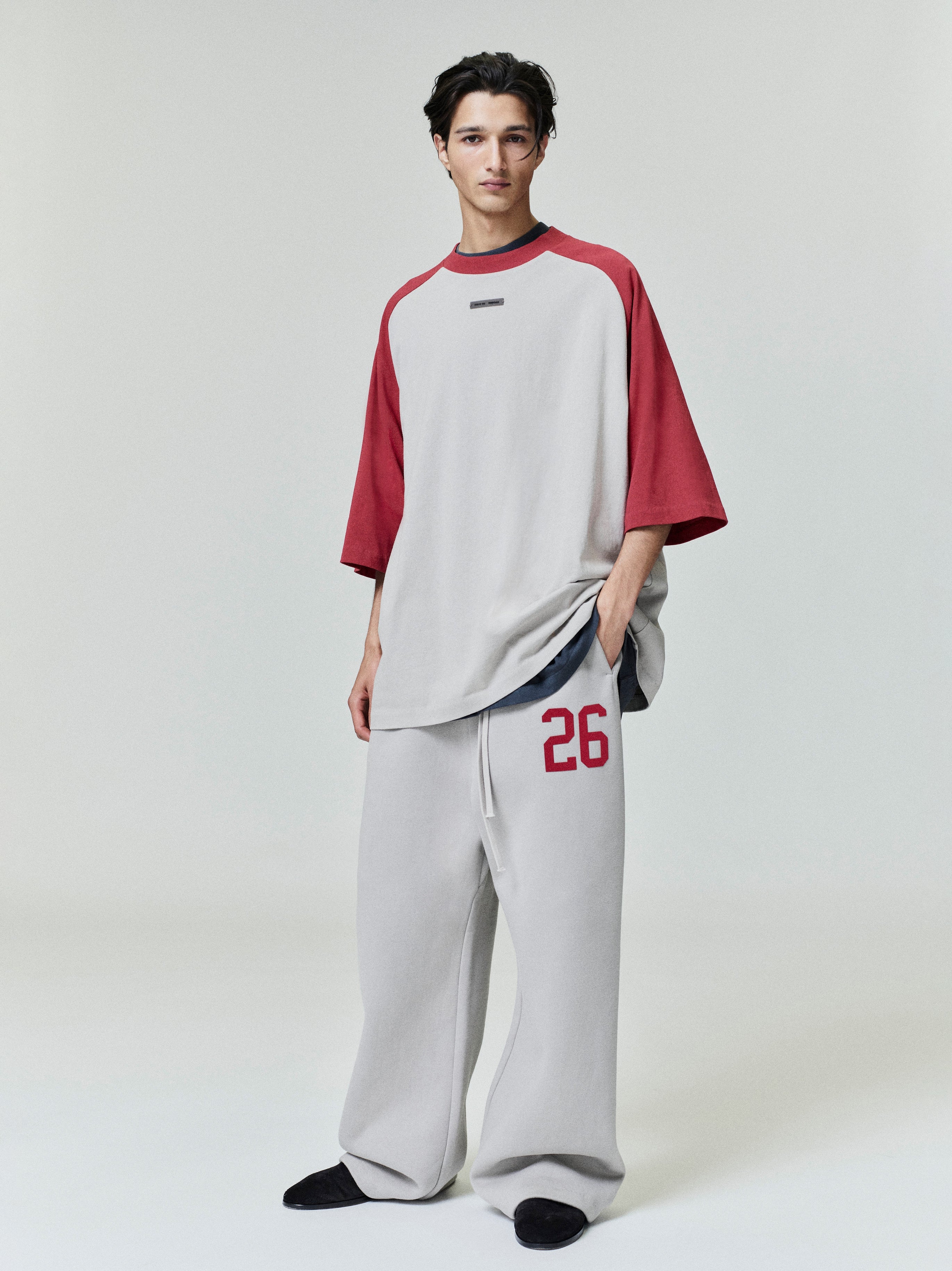 Male model wearing oversized baseball tee with crimson raglan sleeves and light grey body, front view studio shot