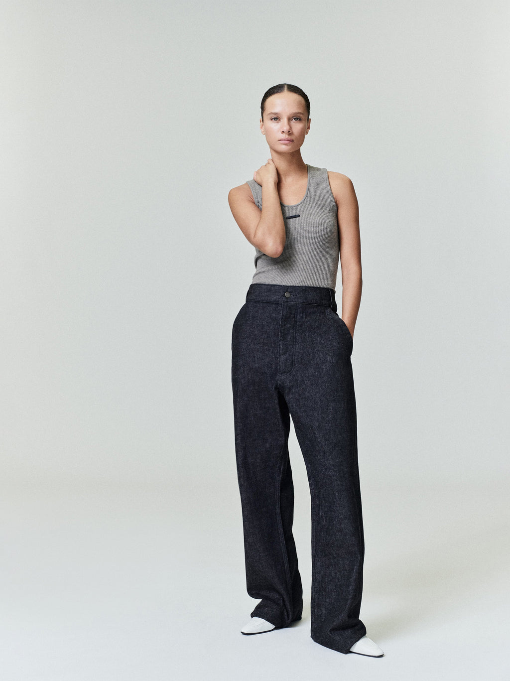 Woman wearing a gray waffle knit tank top with high-waisted loose black pants and white pointed shoes standing straight