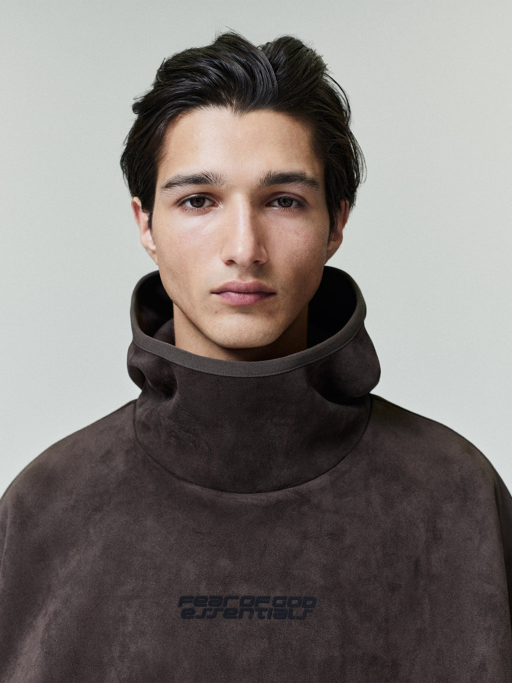 Close-up front portrait of model wearing dark brown suede fleece hoodie with high funnel neck and subtle logo, file 0021_HO25_F.jpg