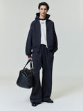 Full-length view of male model wearing black Embroidered Classic Full Zip Hoodie with matching pants and carrying large black tote bag