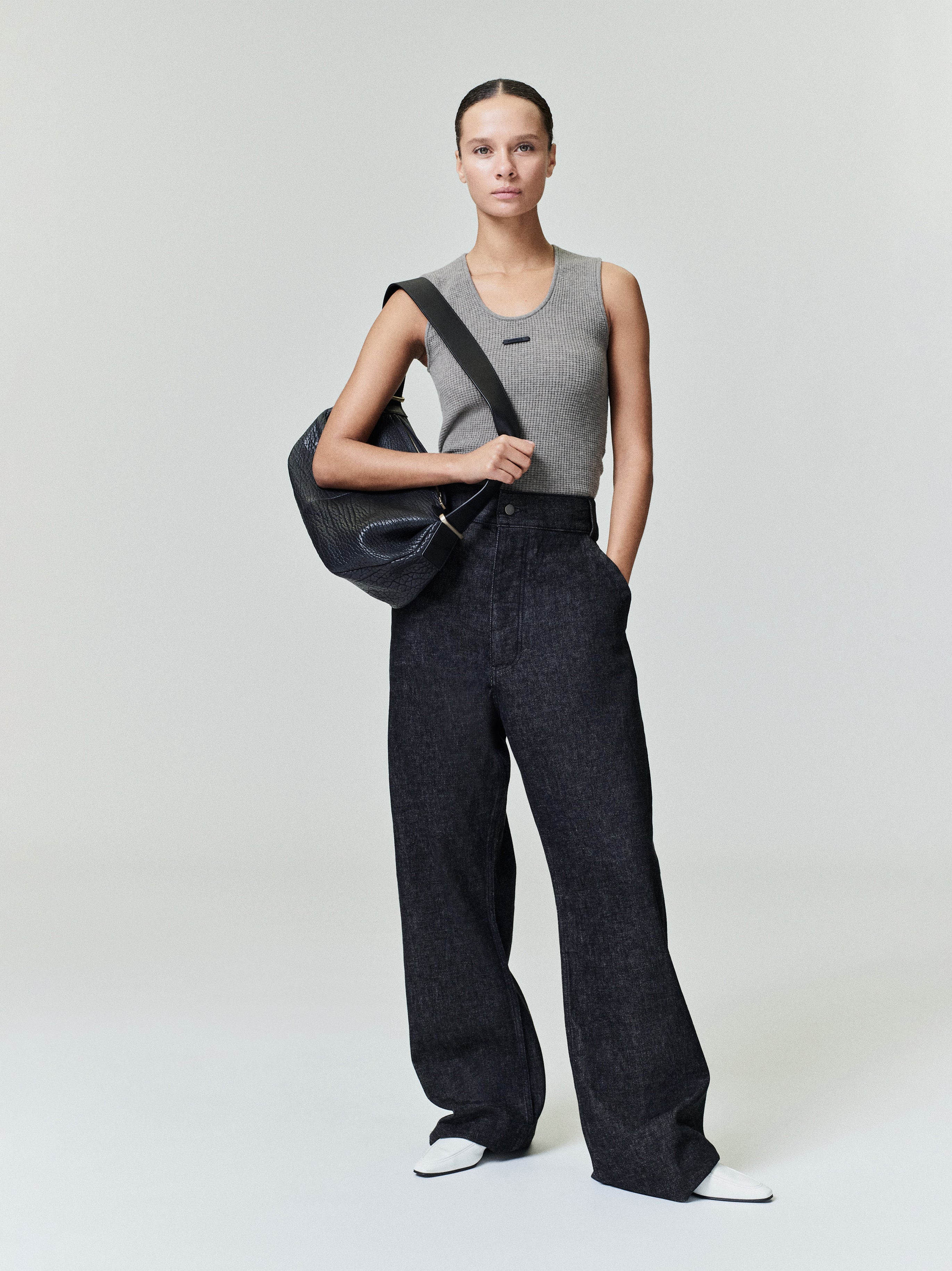Woman wearing a fitted gray waffle tank with wide-leg black pants and carrying a black shoulder bag standing with one hand in pocket