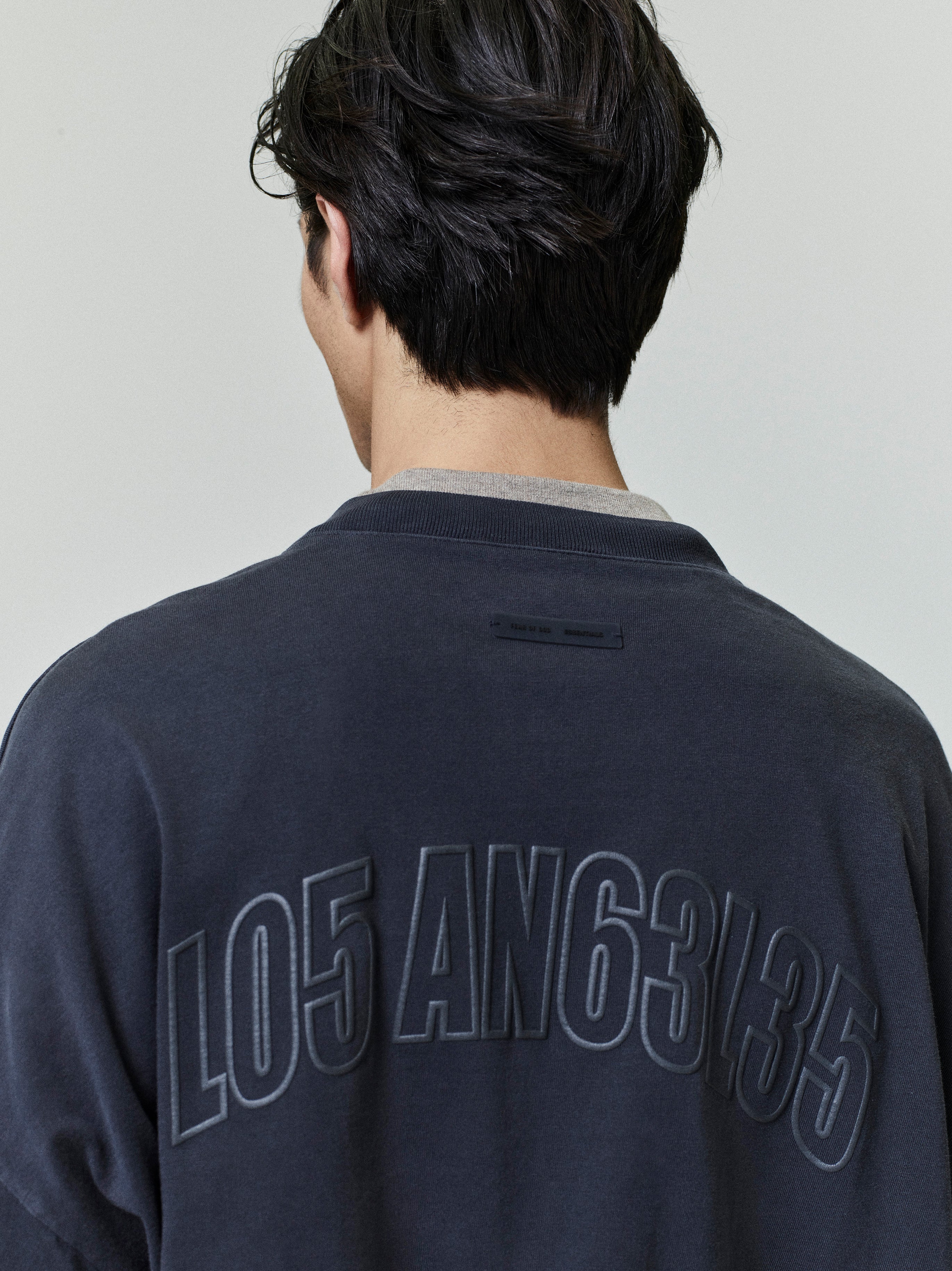 Rear view of man wearing dark Los Angeles 90s Tee with large embossed numeric lettering on back neckline