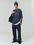 Full body view of model wearing navy Fear of God Essentials 90s Tee with red logo and relaxed fit, styled with black beanie and bag
