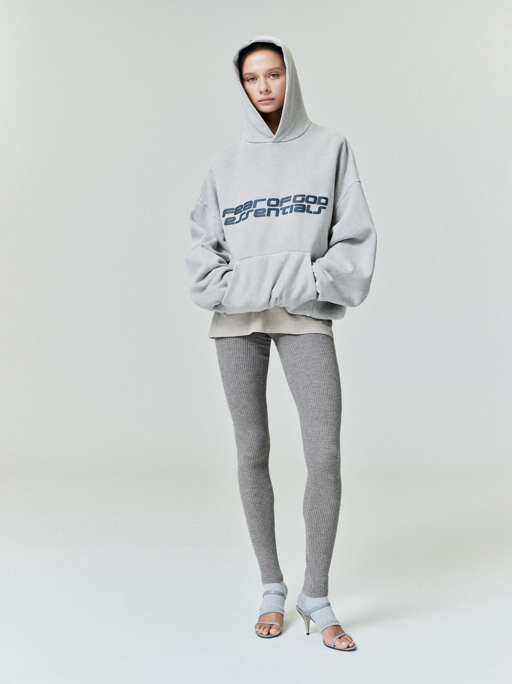 Front view of light gray Heavy Fleece 90s Hoodie with bold Fear of God Essentials logo worn with gray leggings and heels 0030_HO25_FW_L10_P31_1139copy.jpg