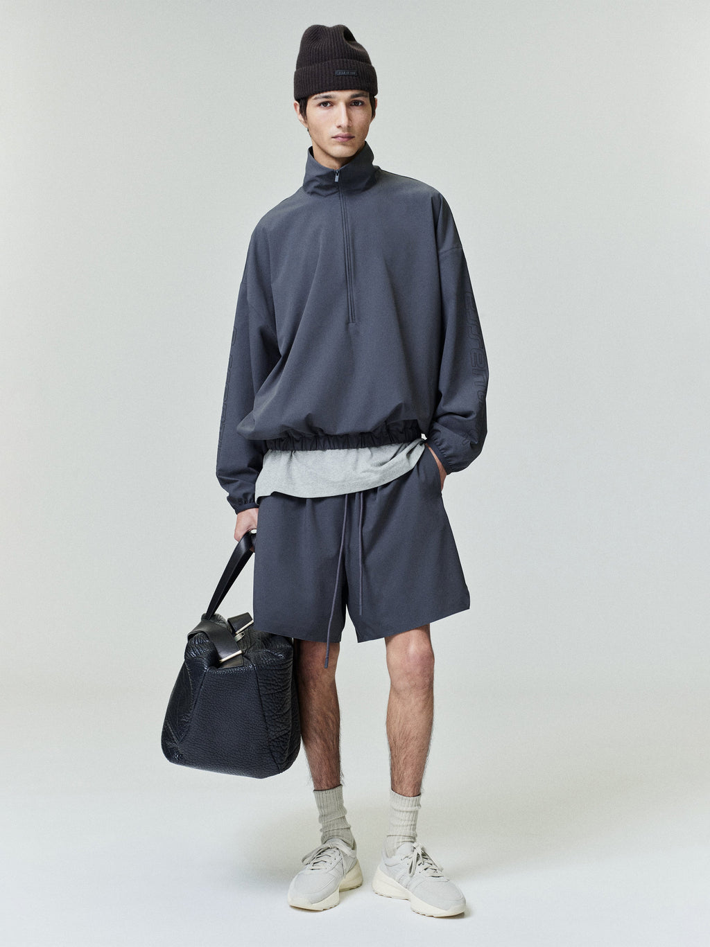 Front view of model wearing dark Tech Nylon Half Zip Track Jacket and matching shorts holding black textured bag, gallery 0