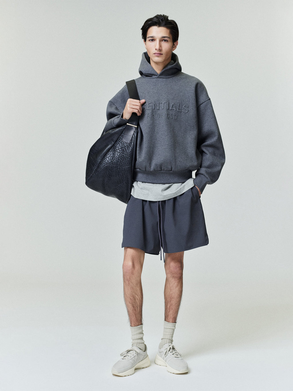 Male model wearing iron grey Tech Nylon Classic Short styled with dark grey hooded sweatshirt and black leather bag