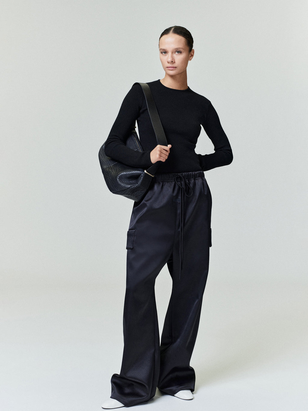 Model standing wearing black Bonded Satin Field Pant with drawstring waistband and straight leg, gallery 0, file 0035_HO25_FW.jpg
