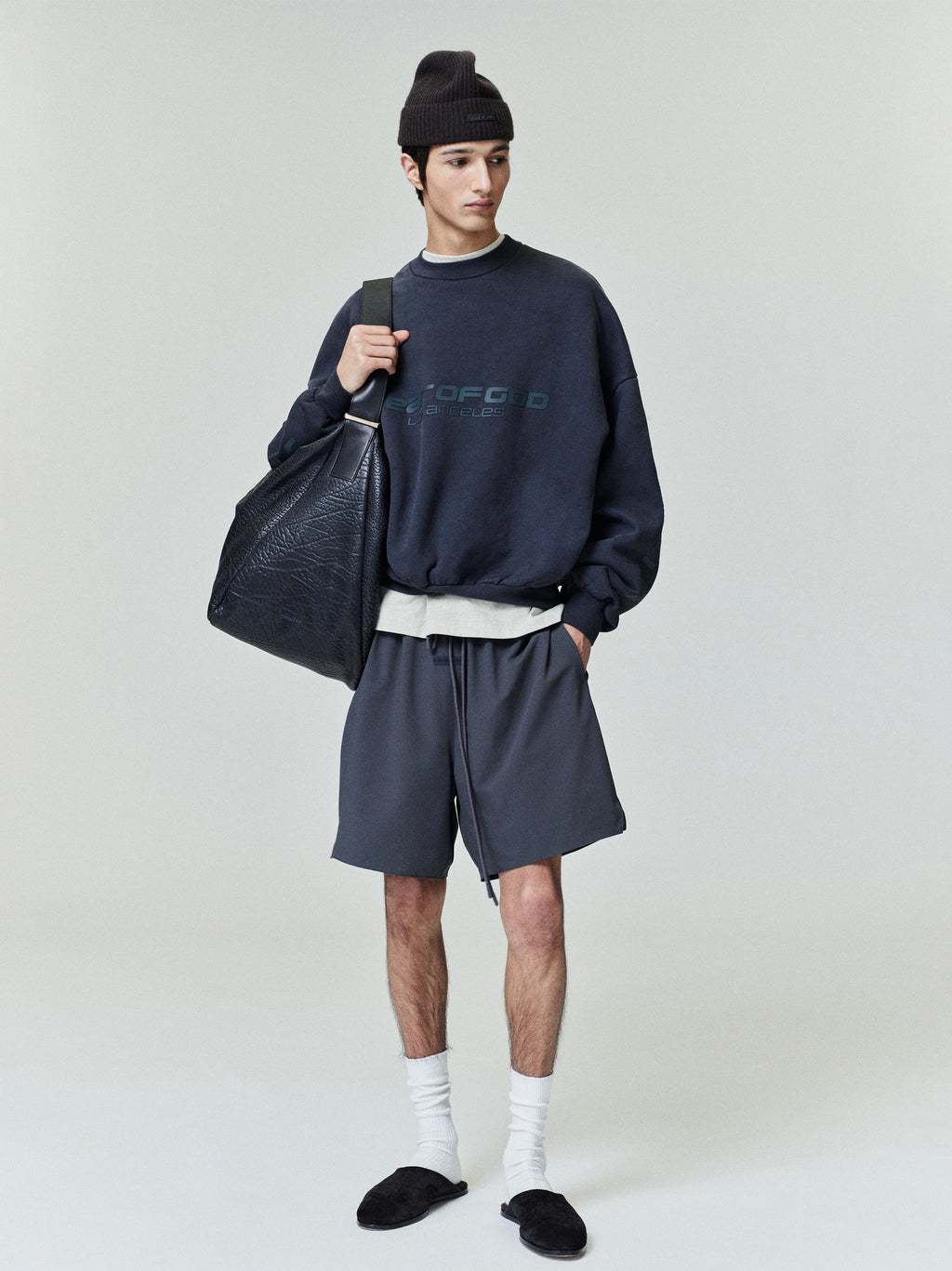 Model wearing iron grey Tech Nylon Classic Shorts standing with black oversized bag in minimalist studio setting