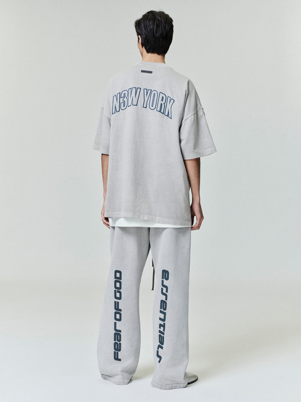 Model wearing oversized light grey New York 90s Tee with navy block lettering and matching wide-leg pants with vertical print