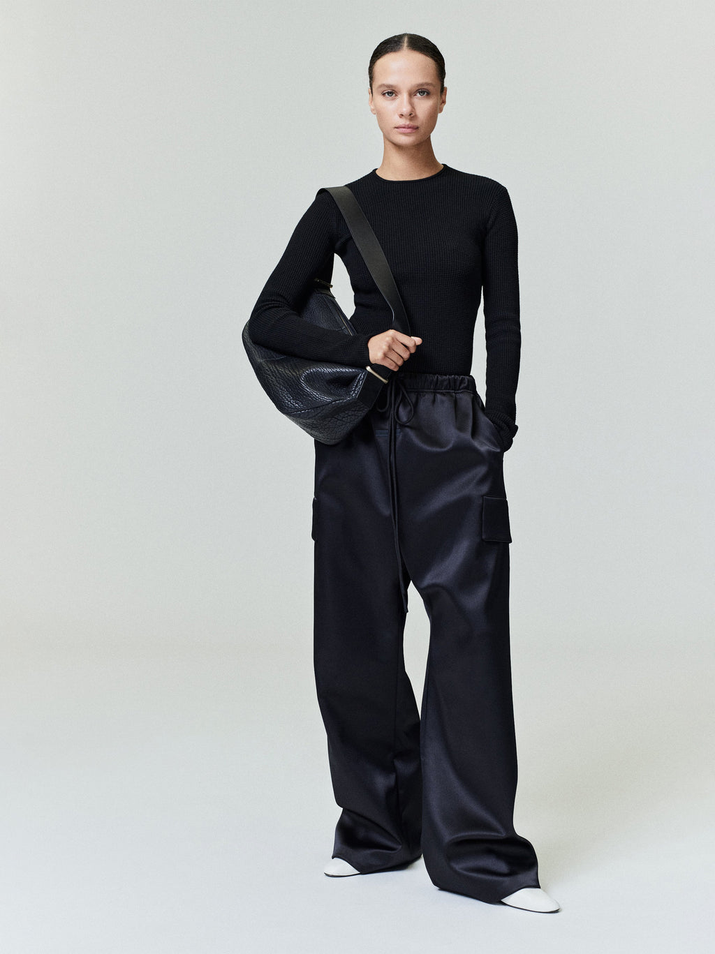 Model wearing black waffle knit long sleeve top with wide-leg black cargo pants and large black leather shoulder bag