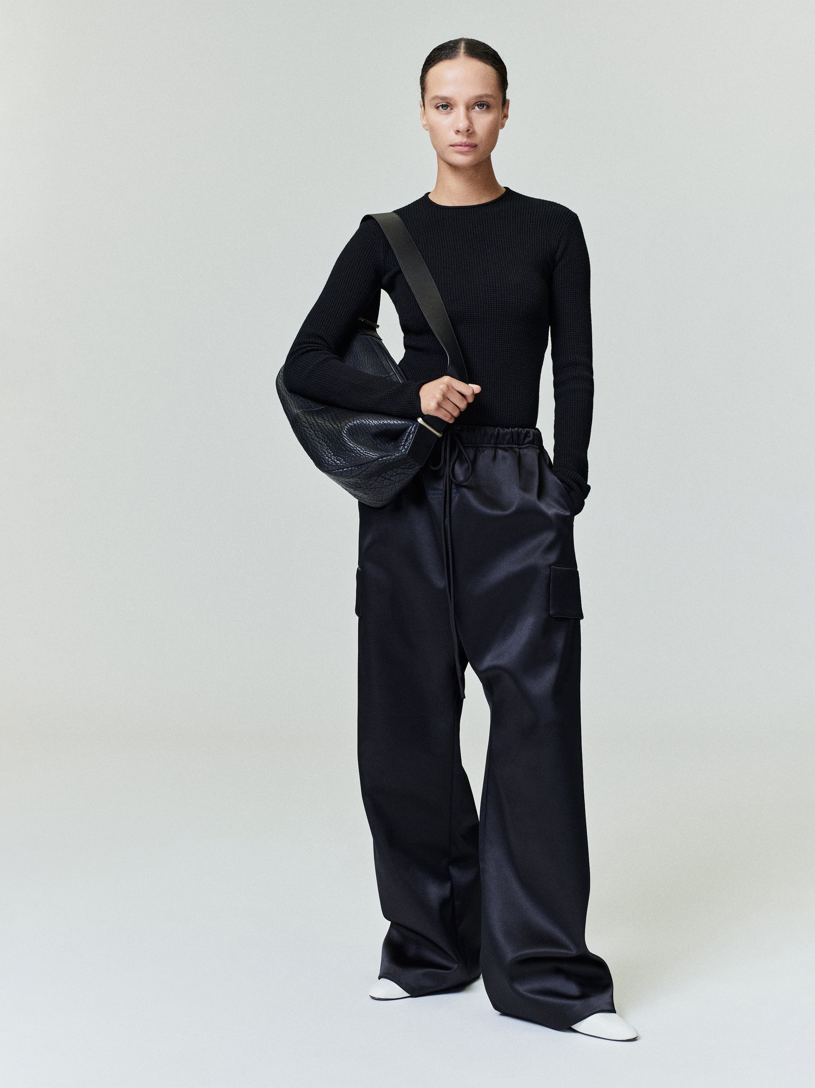 Model wearing black waffle knit long sleeve top with wide-leg black cargo pants and large black leather shoulder bag