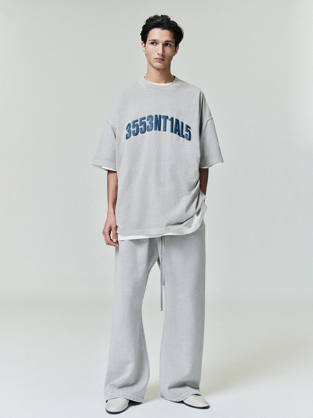 Model wearing oversized light grey New York 90s Tee with navy blue numeric print, paired with matching loose wide-leg pants