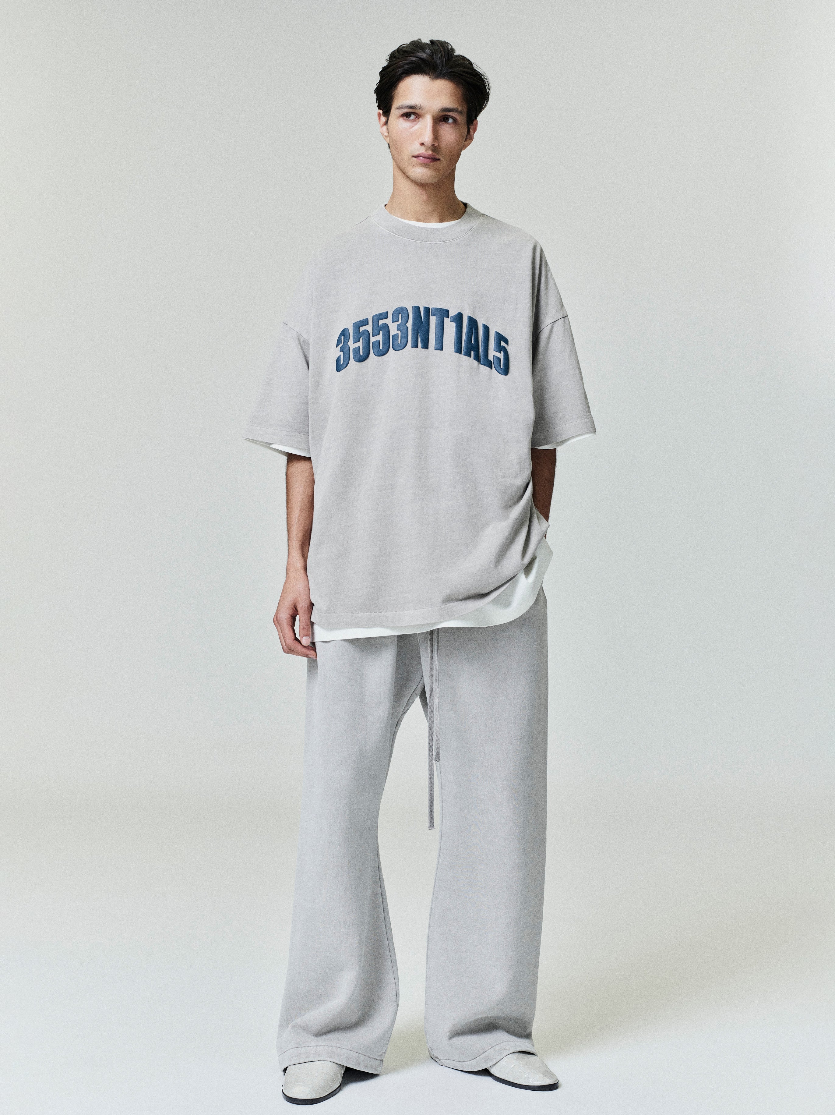 Model wearing oversized light grey New York 90s Tee with navy blue numeric print, paired with matching loose wide-leg pants