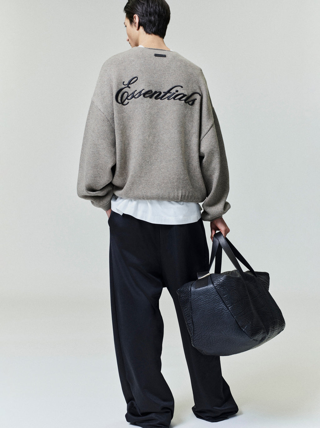 Model wearing black Satin Fleece Lounge Sweatpant with loose fit, paired with oversized sweater and carrying textured black leather bag