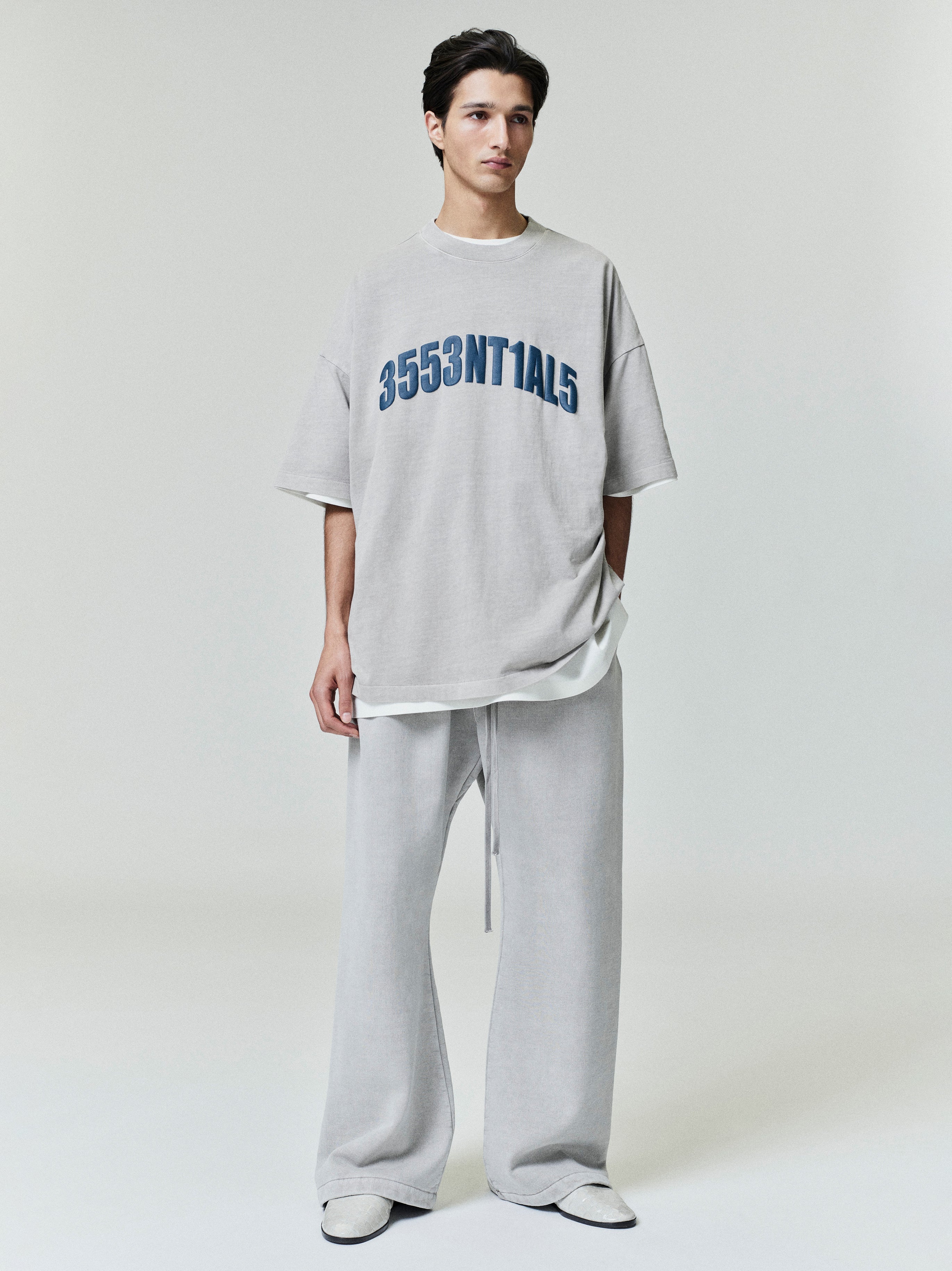 Model wearing oversized light grey New York 90s Tee with blue numeric print paired with matching loose wide-leg pants