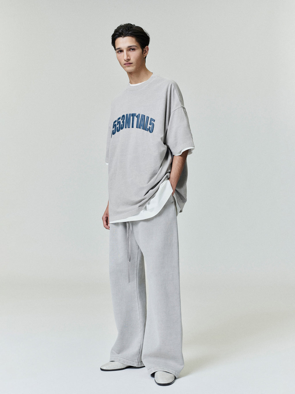 Standing model wearing light grey New York 90s Tee with navy alphanumeric print and matching relaxed wide-leg pants