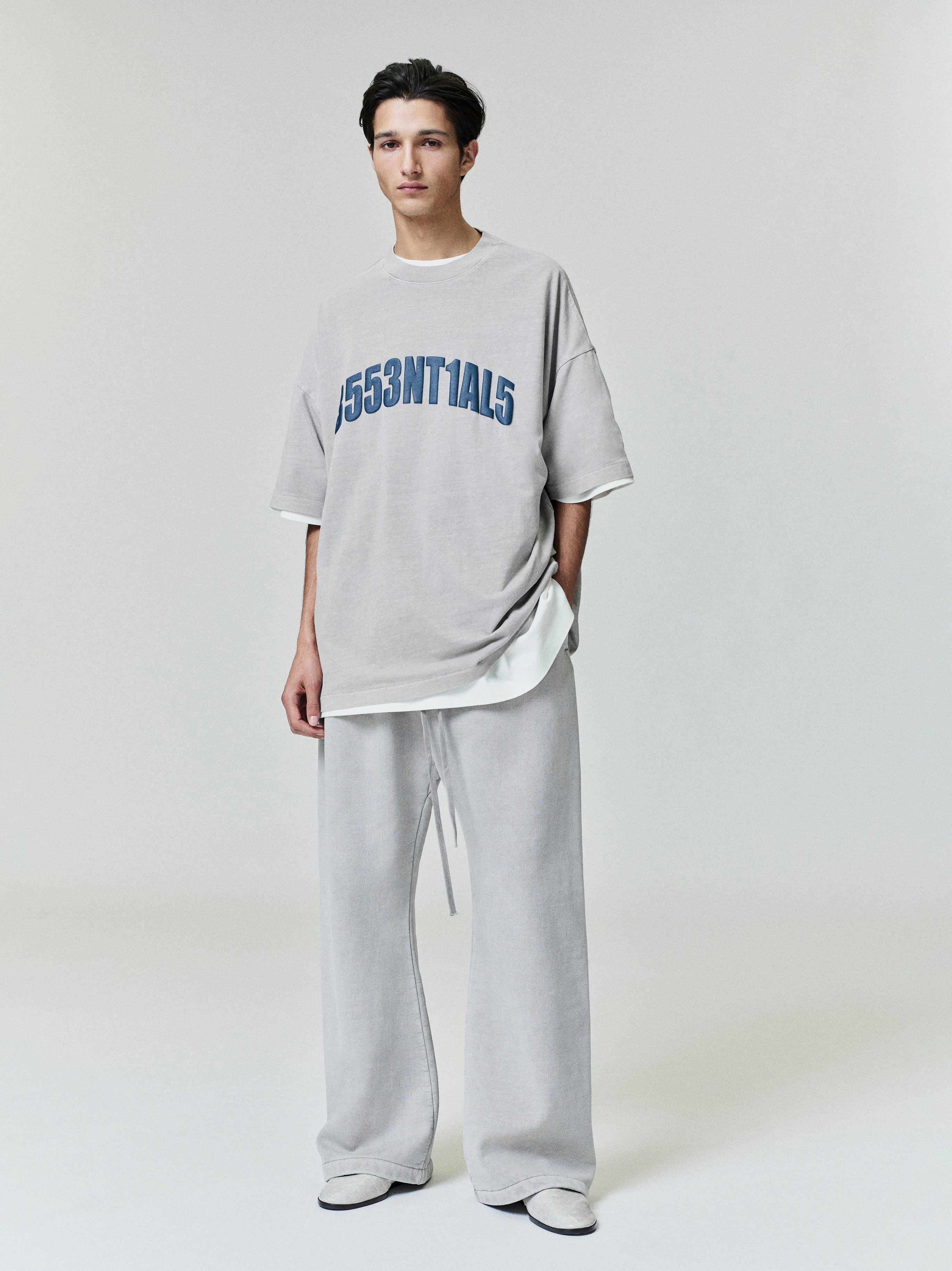 Full-length view of light grey New York 90s Tee with bold blue alphanumeric print worn with matching wide-leg pants