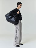 Side view of model wearing light gray Heavy Fleece Lounge Sweatpant with large black side script graphic and black oversized bag