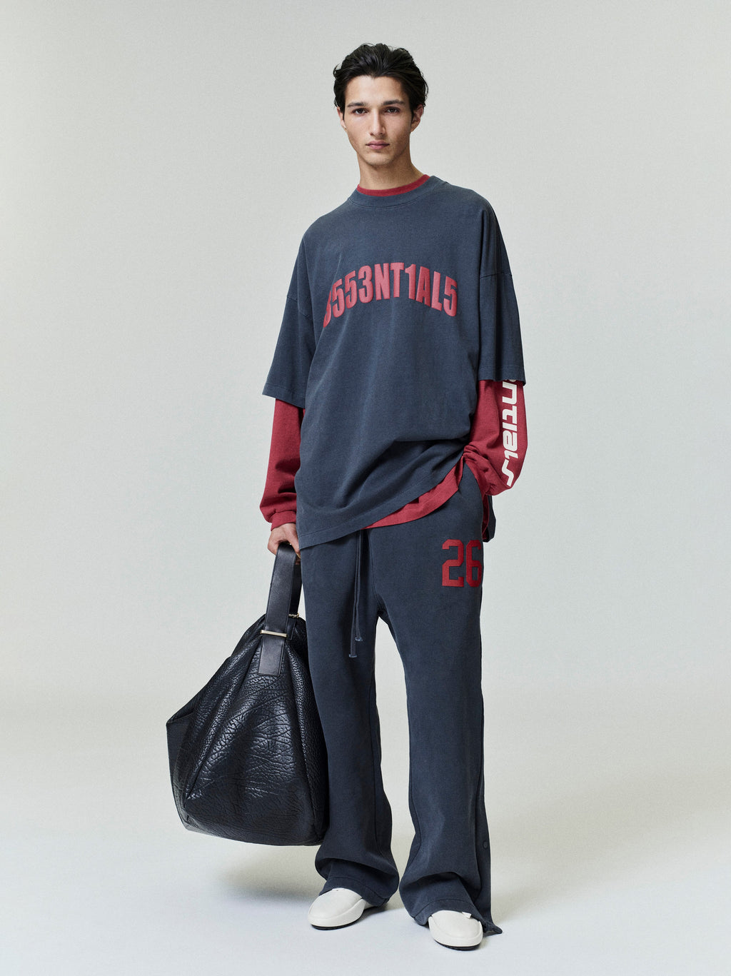 Full-length photo of model wearing dark Chicago 90s Tee layered over red long-sleeve top with matching pants and black leather bag