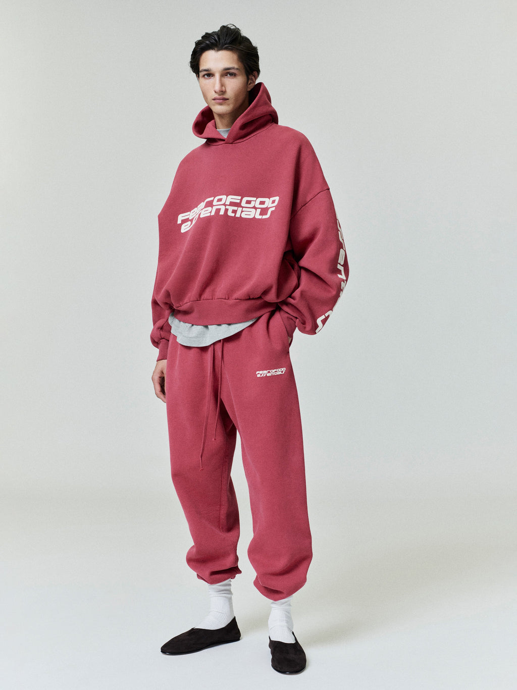 Full body front view of model wearing crimson cropped relaxed hoodie with white Fear of God Essentials logo on chest and sleeves