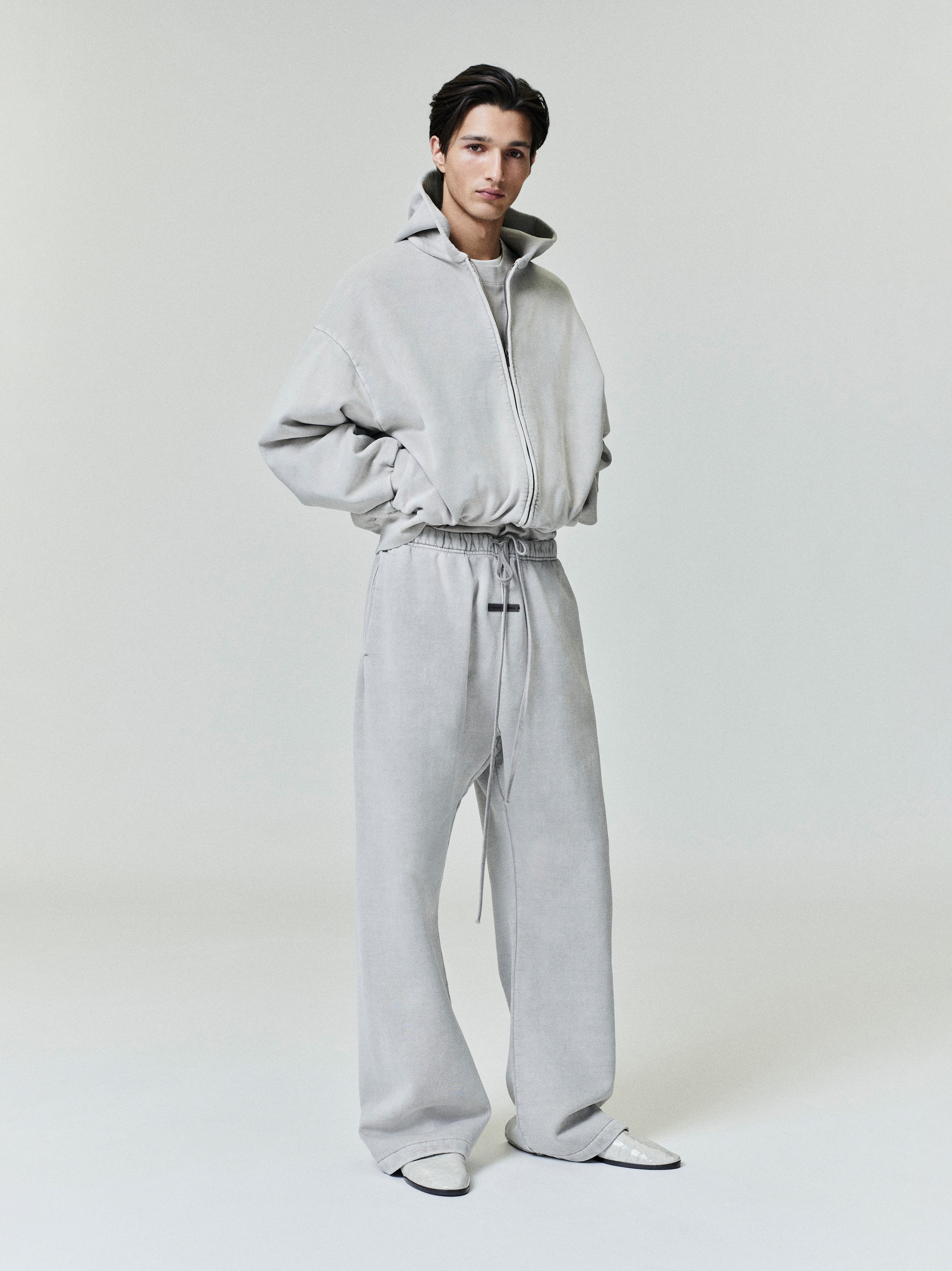 Full-length shot of model in light grey Embroidered Classic Full Zip Hoodie with relaxed fit and matching pants on plain background