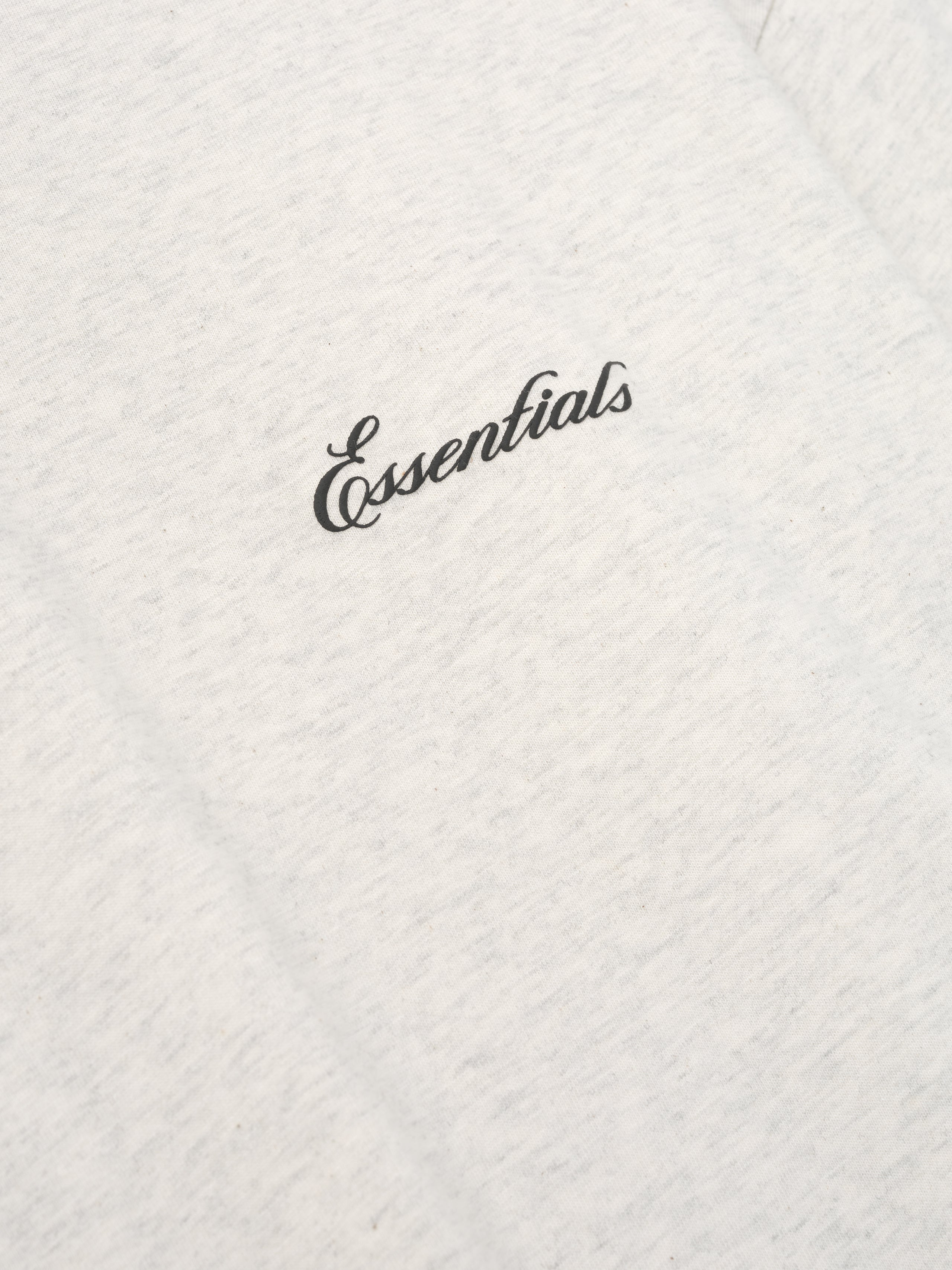 off-white cotton jersey fabric close-up with black Essentials script logo on chest of long sleeve tee
