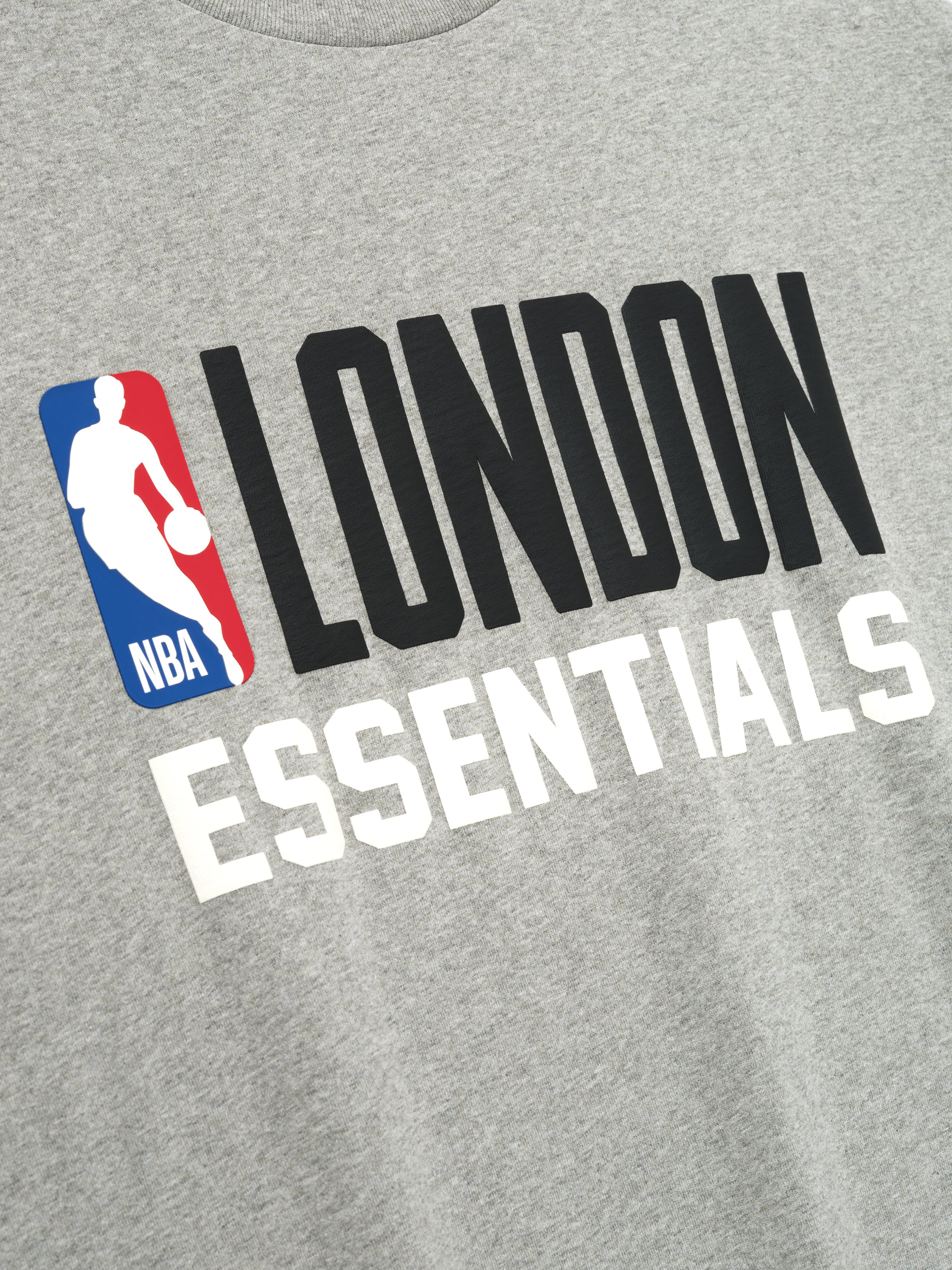 Close-up of concrete heather fabric with bold black LONDON and white ESSENTIALS text and NBA logo on front of tee, file 125EU264202F