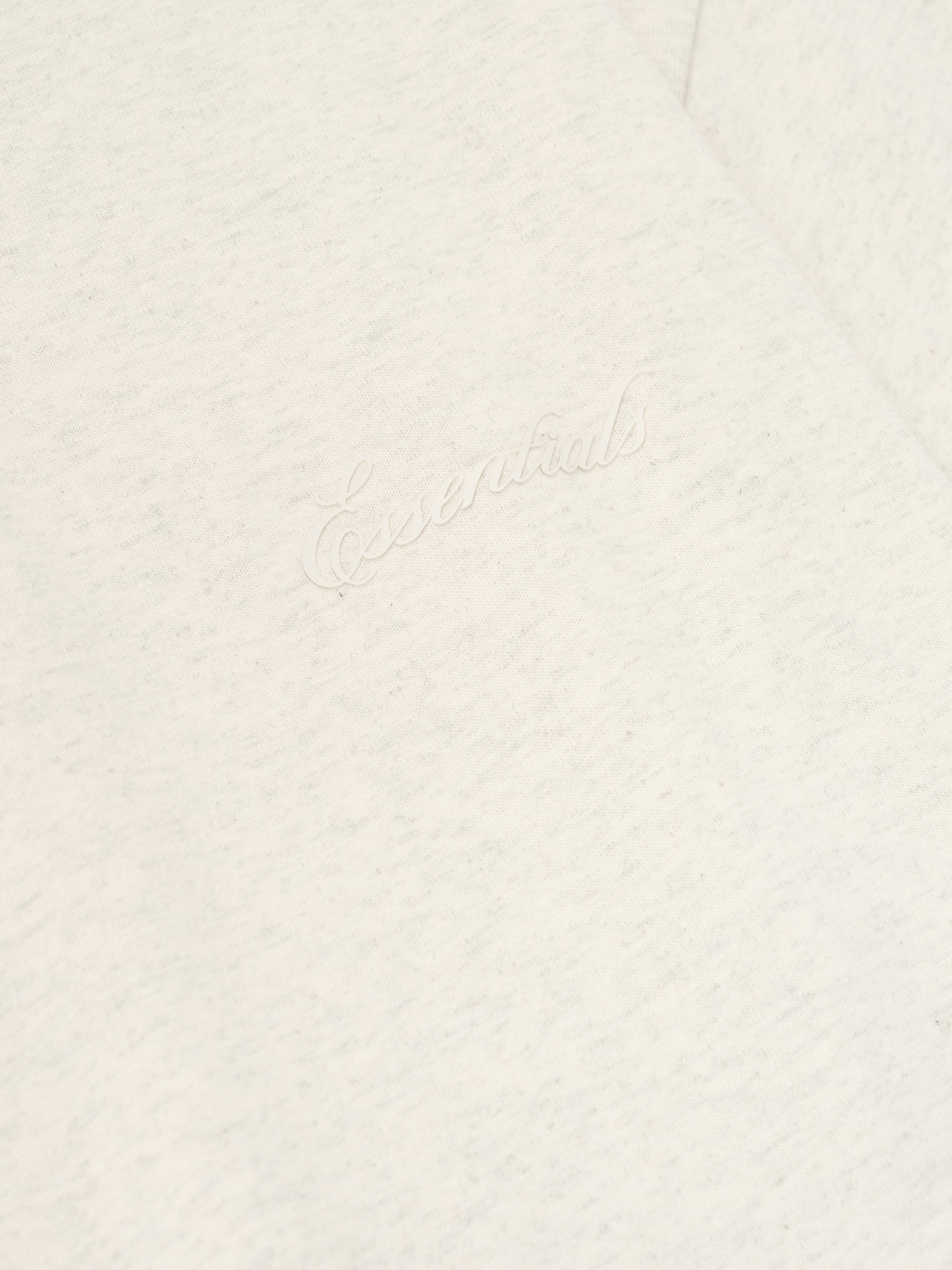 Close-up of oatmeal heather Embroidered Classic Short Sleeve Tee highlighting tonal "Essentials" script embroidery on chest area