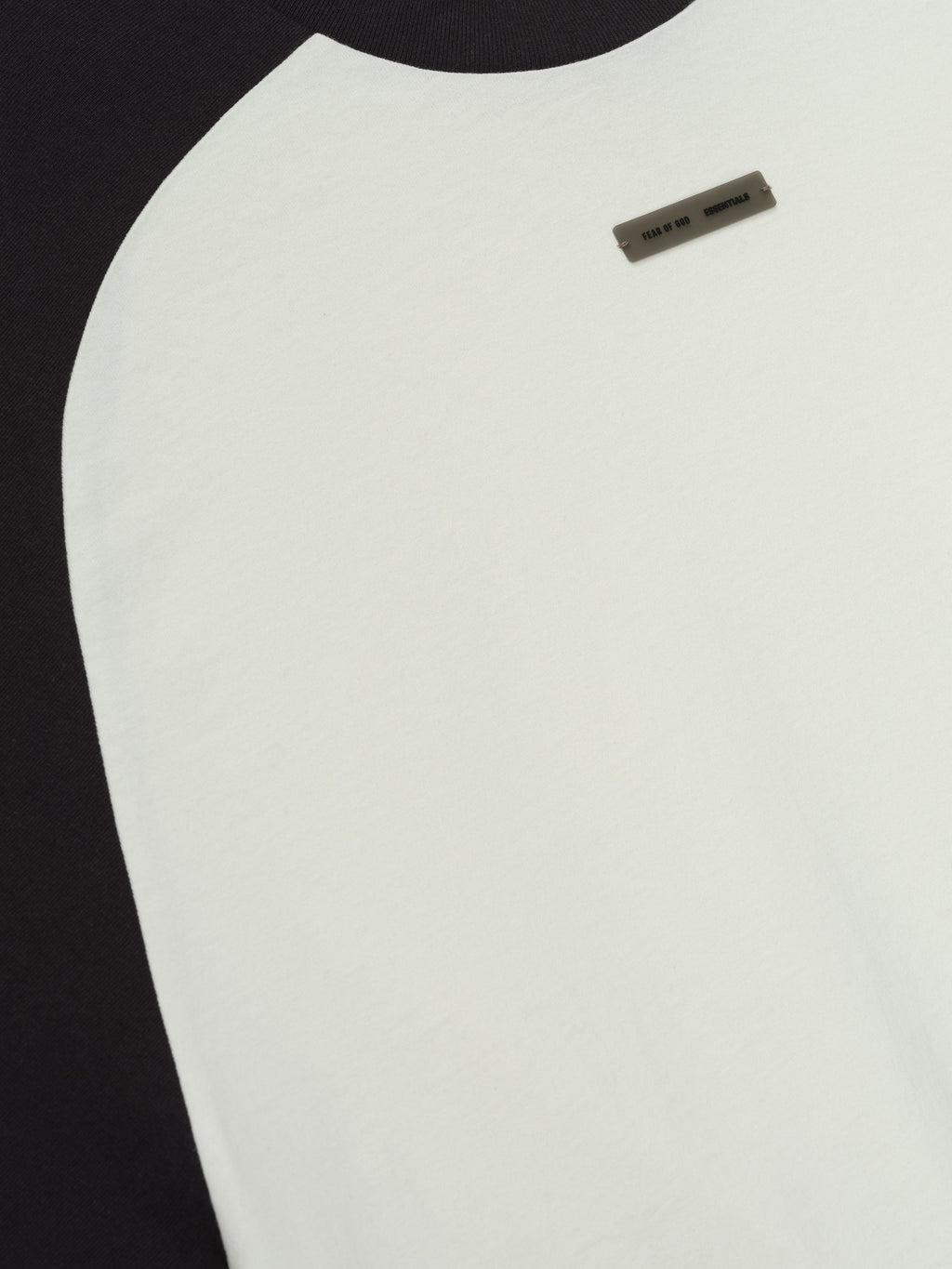 Close-up of ivory baseball tee with black raglan sleeves and small rectangular label near neckline, front detail view.