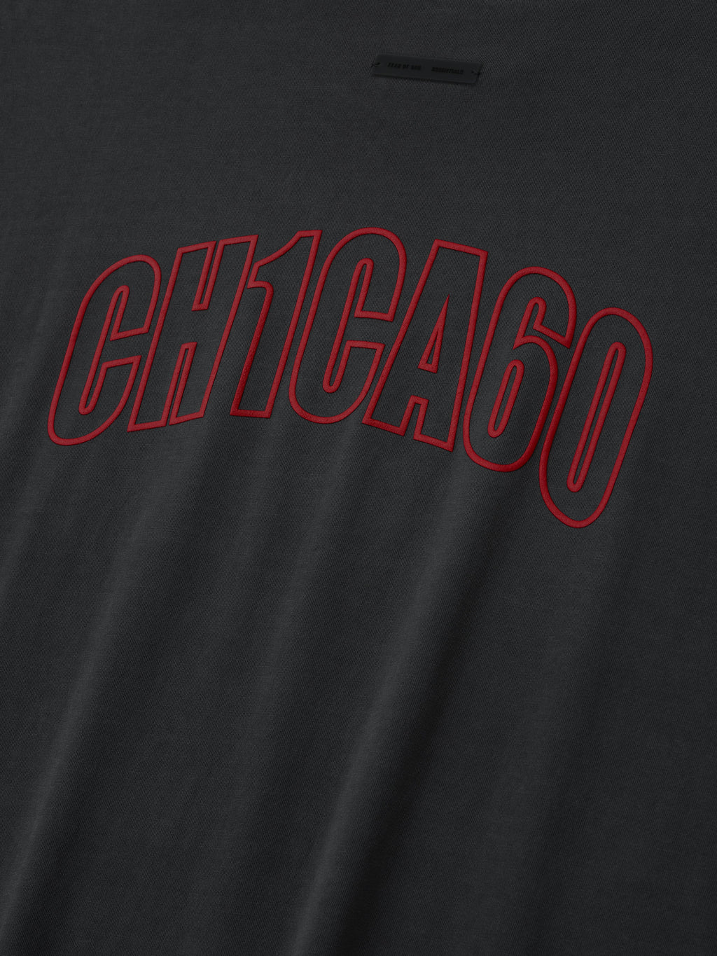 Close-up of iron grey Chicago 90s Tee with bold red outlined CH1CA60 print on soft fabric surface