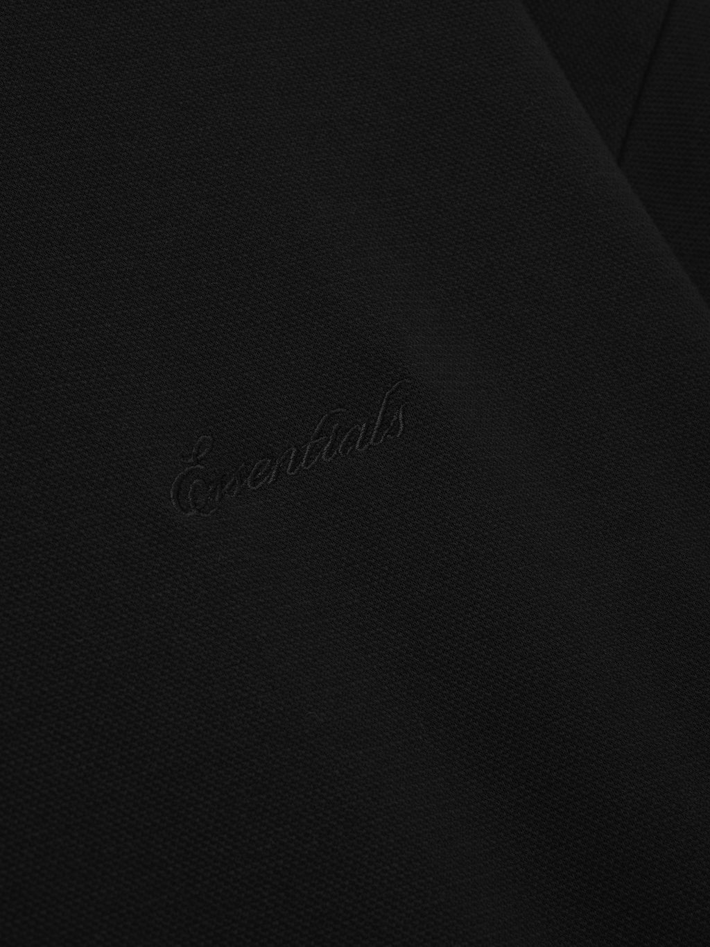close-up of black medium-weight cotton poly pique fabric with subtle embossed Essentials signature branding