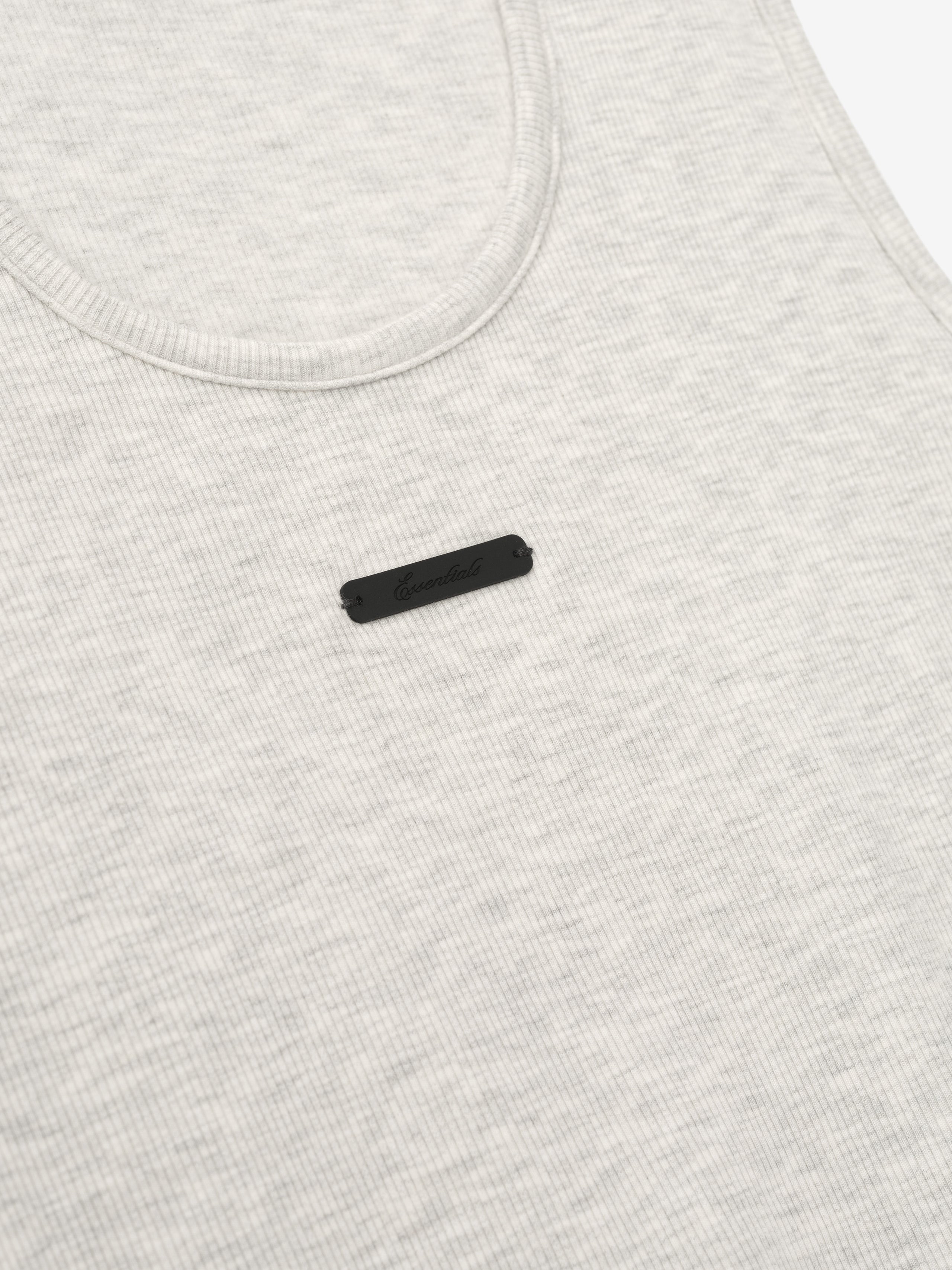 close-up of light cream ribbed cotton-rayon-spandex tank top with U-neck and small black logo patch on chest