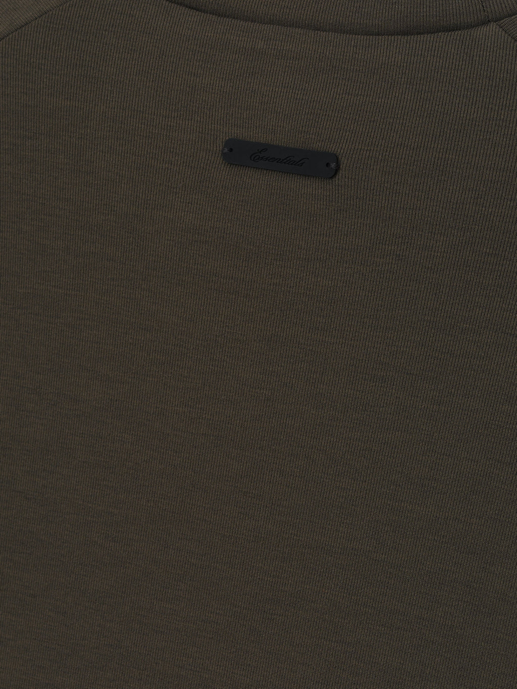 close-up of dark olive ribbed knit fabric with small black Essentials logo patch sewn near neckline
