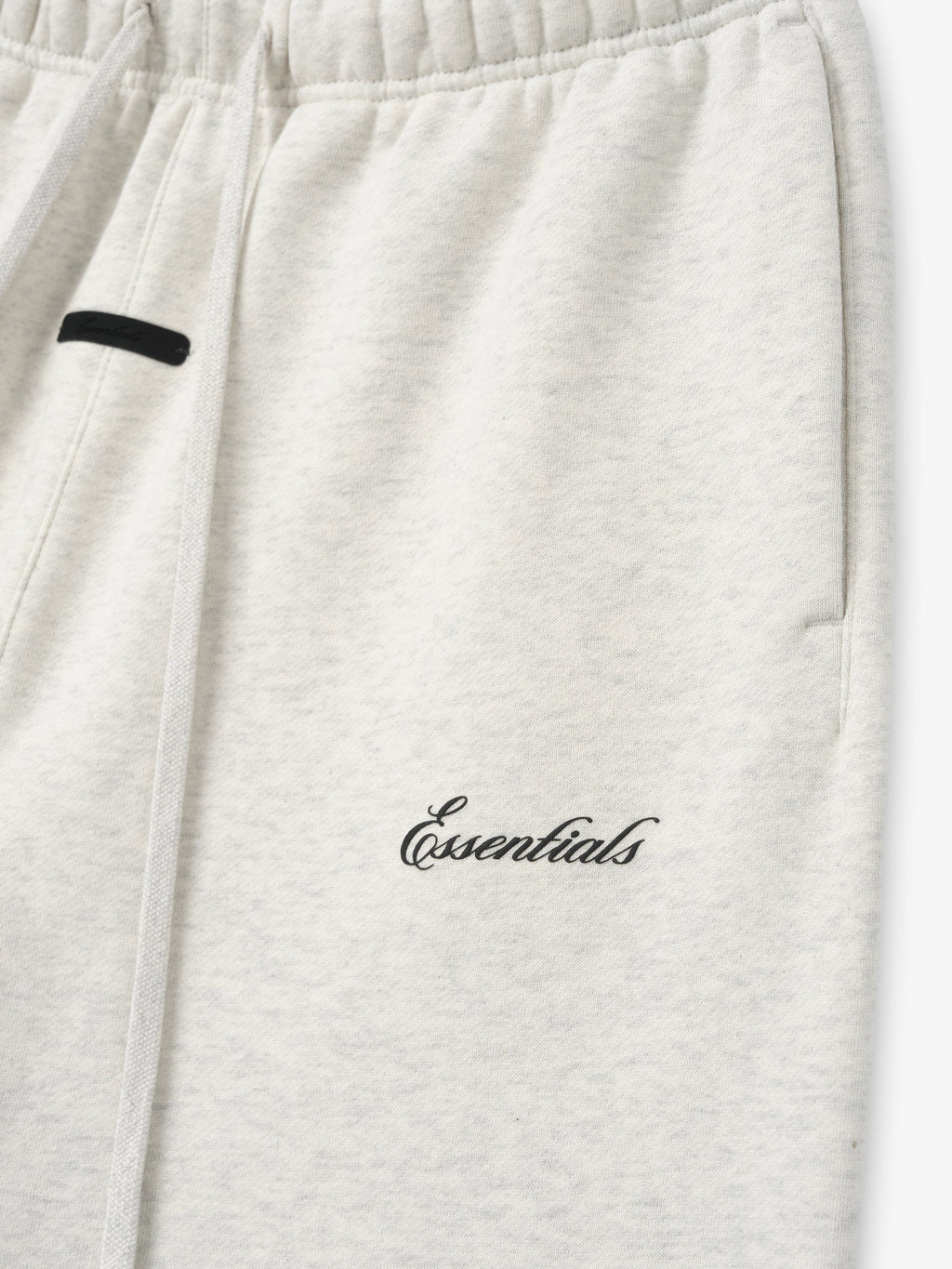 close-up of light heather gray sweatpant with elastic waistband and black puff-printed Essentials logo on thigh