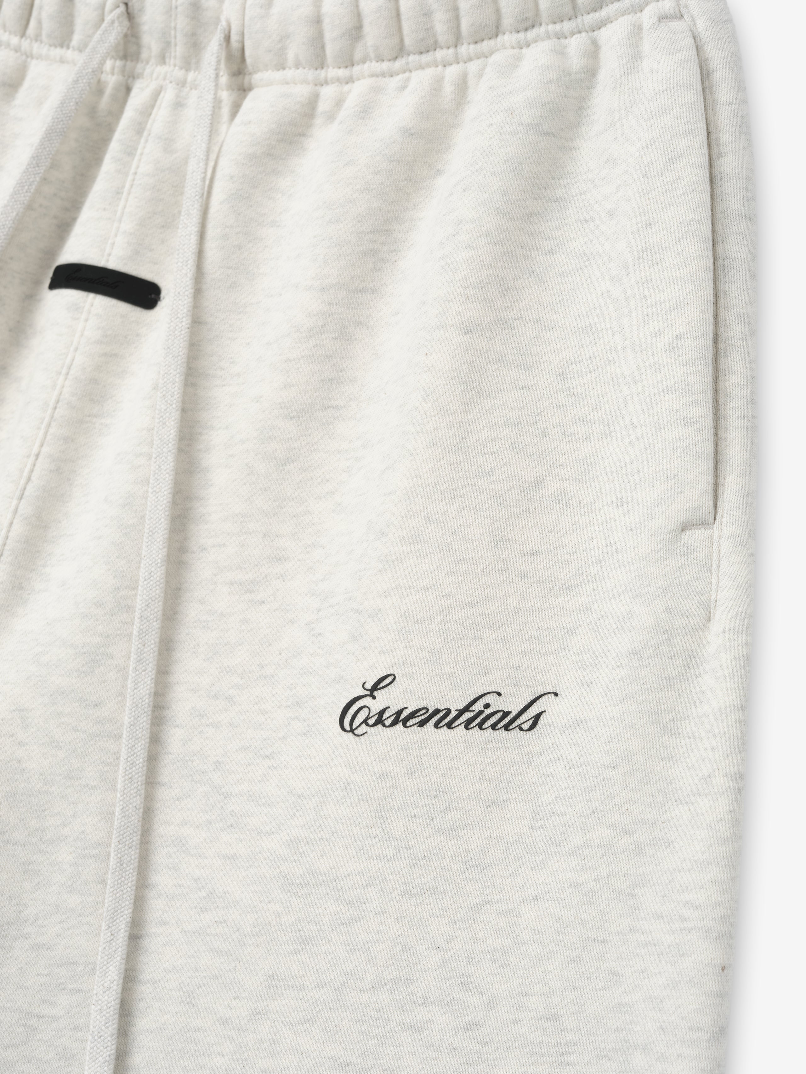 close-up of light heather gray sweatpant with elastic waistband and black puff-printed Essentials logo on thigh